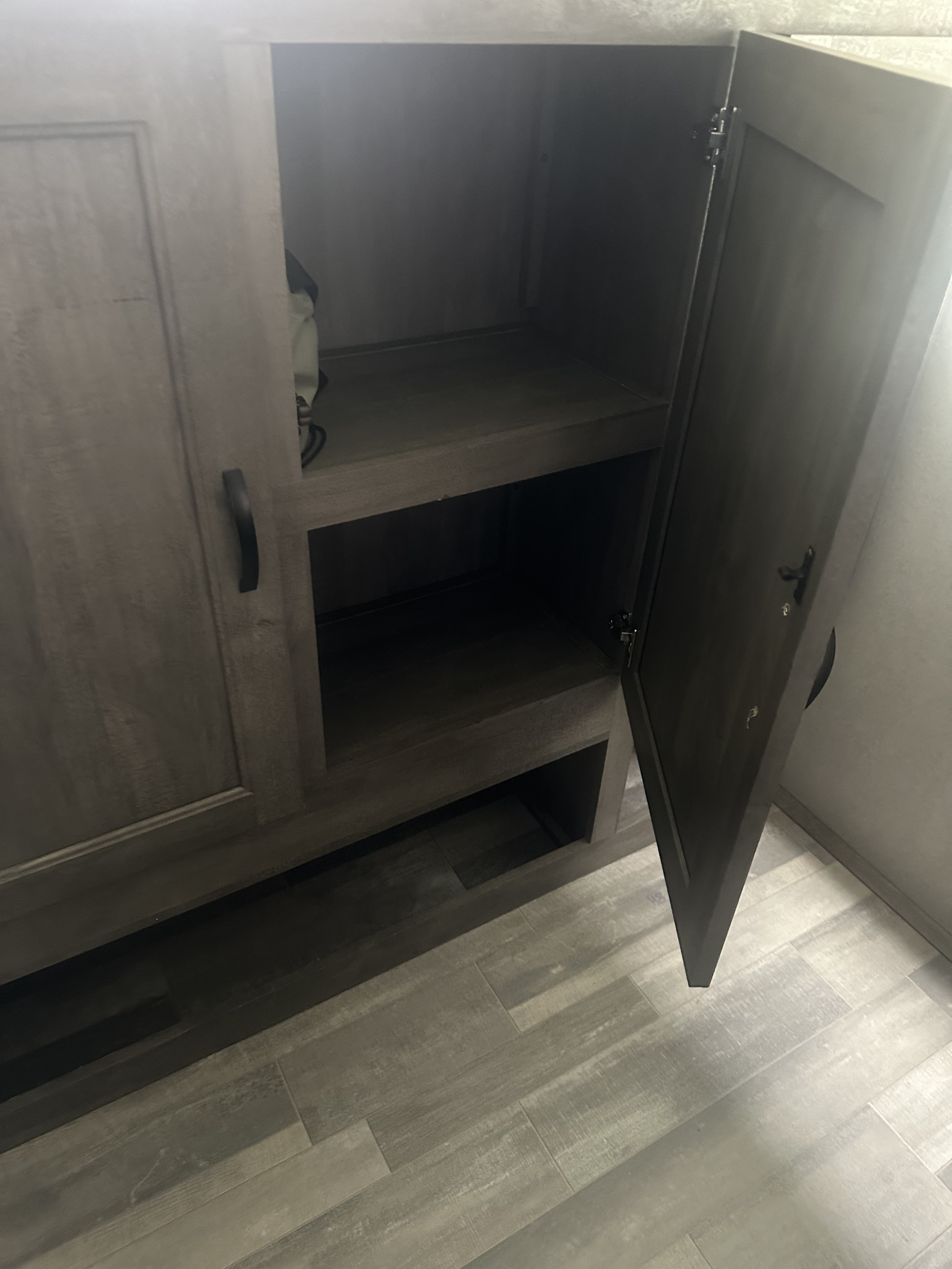 Open RV rental cabinet showcasing two empty shelves and modern wood-look flooring. Provides essential storage space.. Forest River Vibe 2019