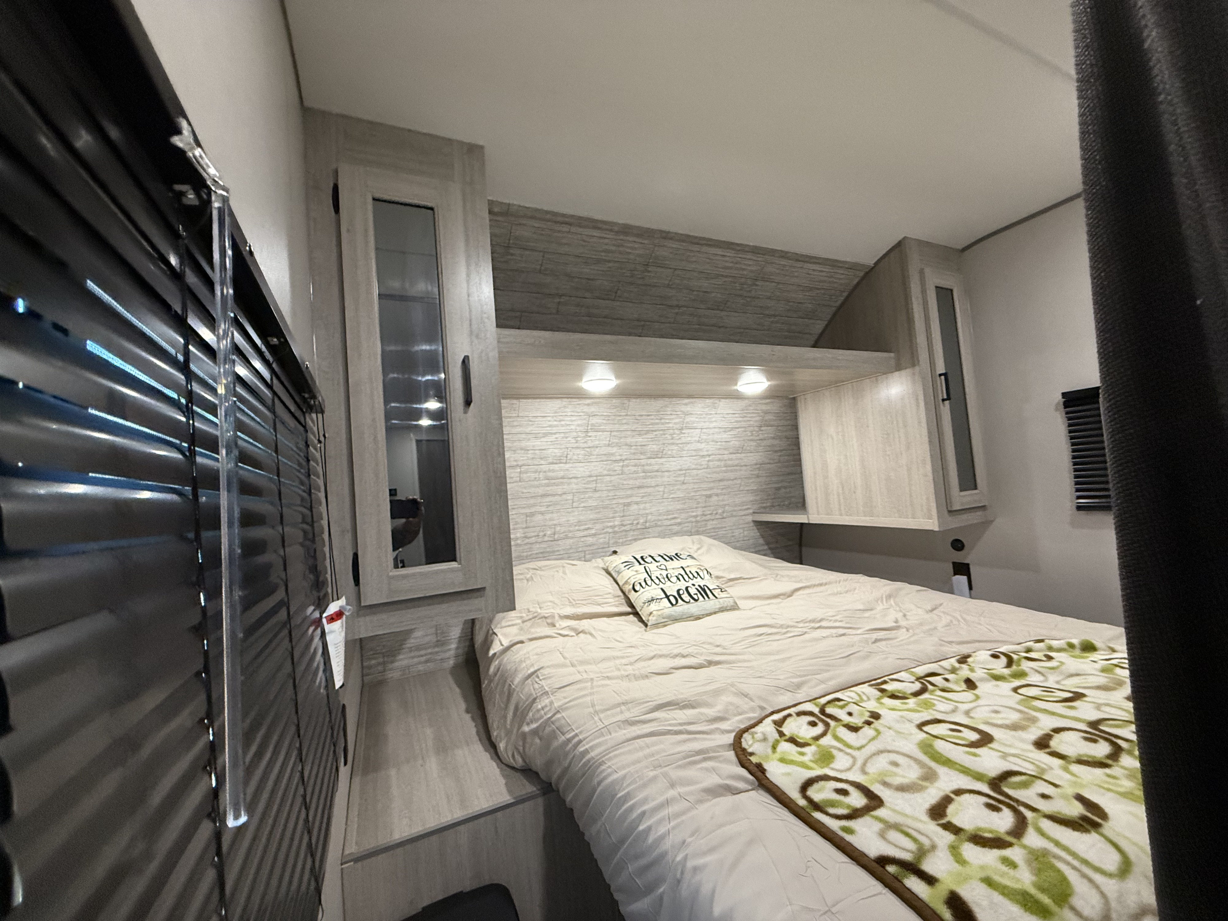 RV rental bedroom: cozy bed with storage, blinds, and reading lights. "Let the adventure begin" pillow.. Coachmen Catalina 261BHS 2025