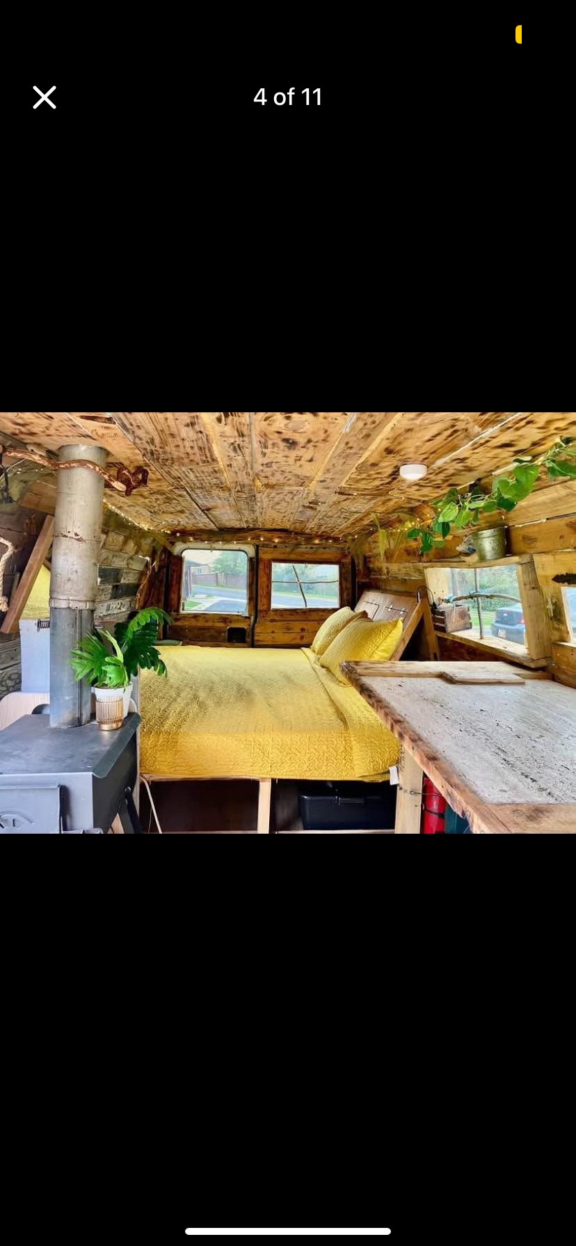 Rustic wood-paneled interior of an RV rental: features a cozy yellow bed, small wood stove, and custom wooden details.. Ford Econoline 2002