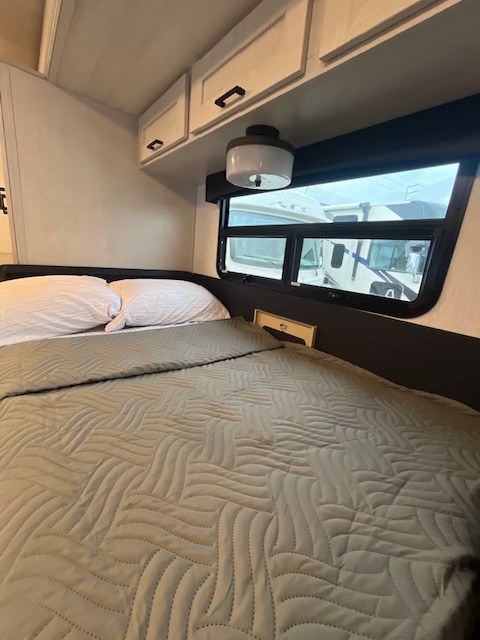 Cozy RV rental bedroom with a comfortable bed, white pillows, overhead cabinets, and a window view, perfect for travel.. Nexus Viper 2026