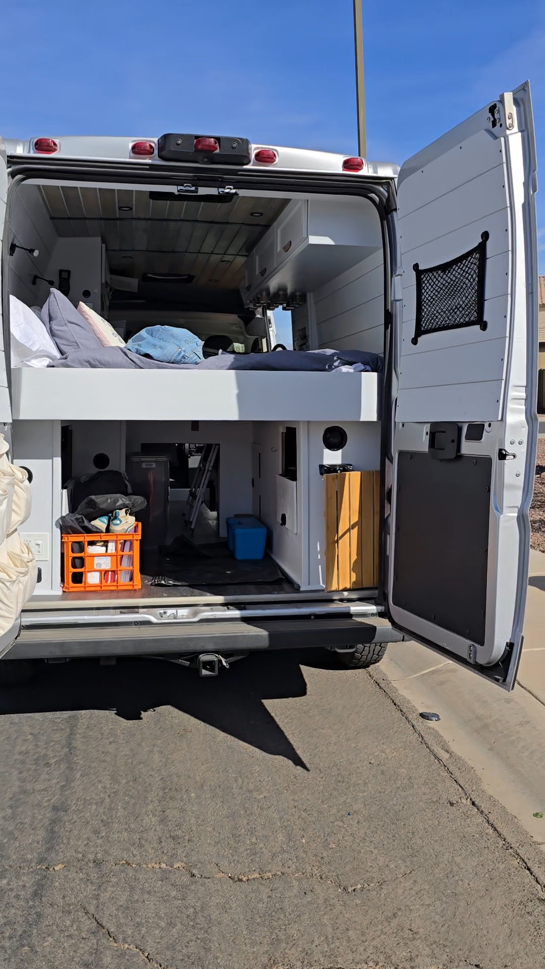 Back of an RV rental camper van with doors open, showcasing a bed above practical storage.. Ram Promaster 2500 2022