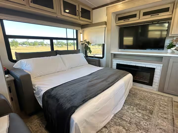Cozy RV rental interior featuring a comfy bed, large windows, and entertainment unit with TV & fireplace. Perfect for travel!. Forest River Flagstaff Classic 2024