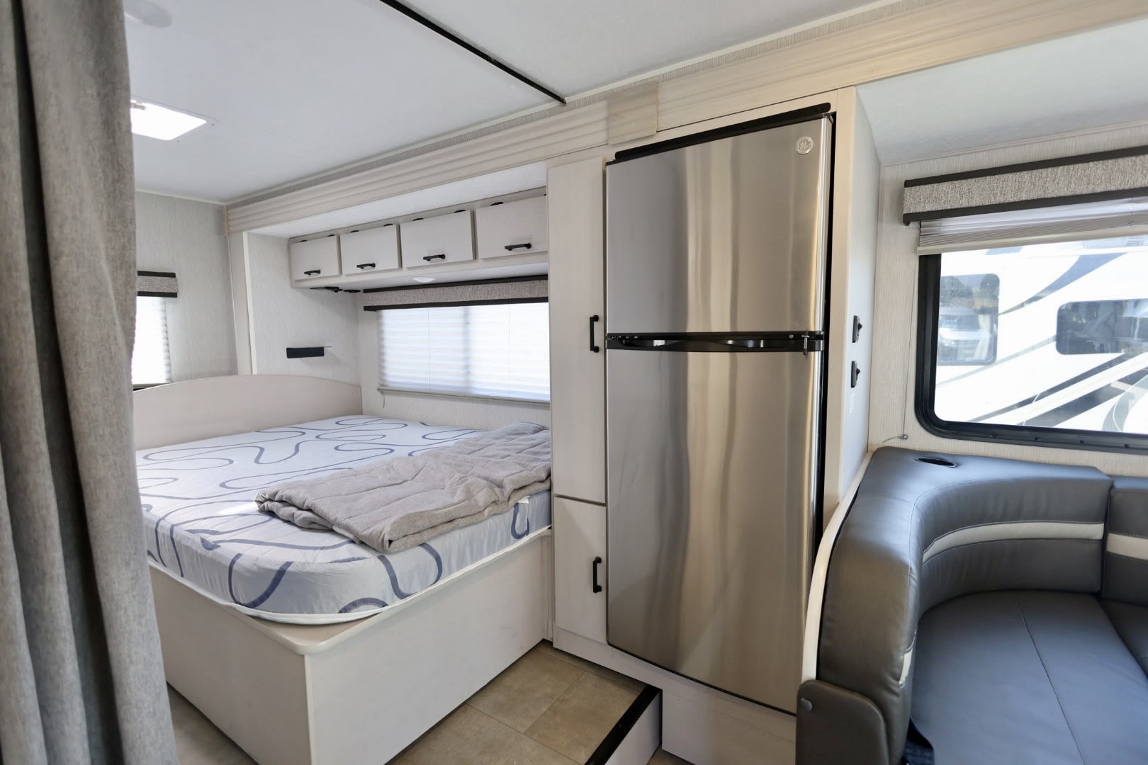 Inside an RV rental: a modern bedroom with storage, a large fridge, and a comfortable lounge area.. Coachmen Freelander 2023