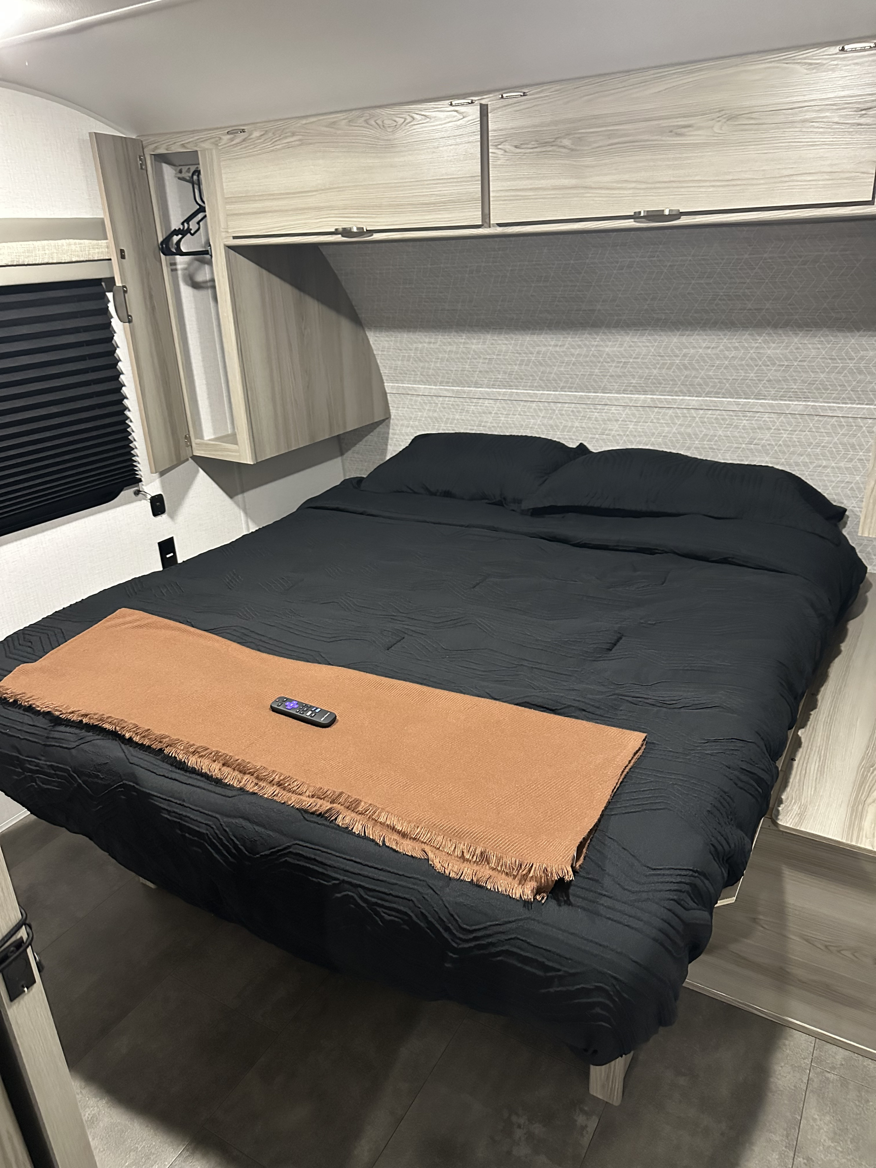 Modern RV rental bedroom with a black bed, rust throw, remote, overhead storage, and pleated blinds.. Forest River Salem Cruise Lite 2024