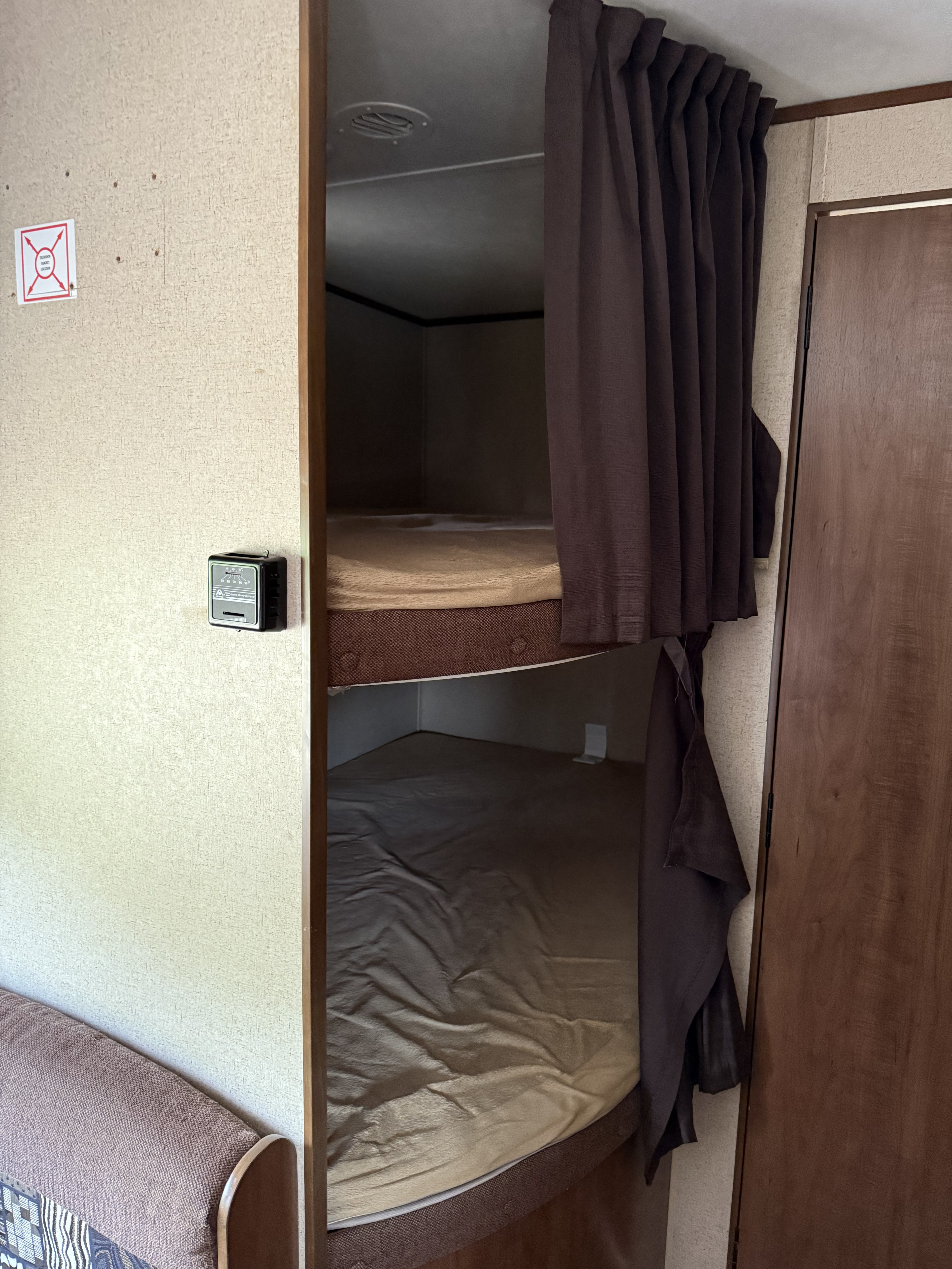 Bunk beds with privacy curtains in an RV rental interior. Note the thermostat and TV bracket location on the wall.. Jayco Jay Flight SLX 2016