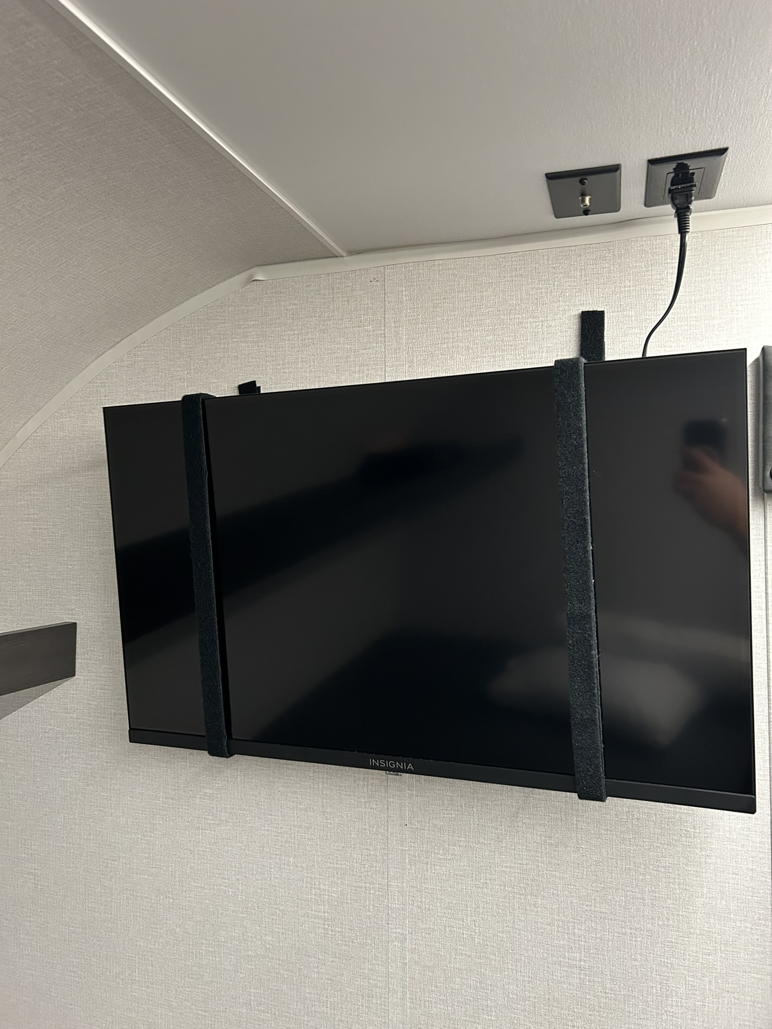 Wall-mounted Insignia TV in an rv rental, secured by straps. Shows power and cable connections above.. Heartland Prowler 2025