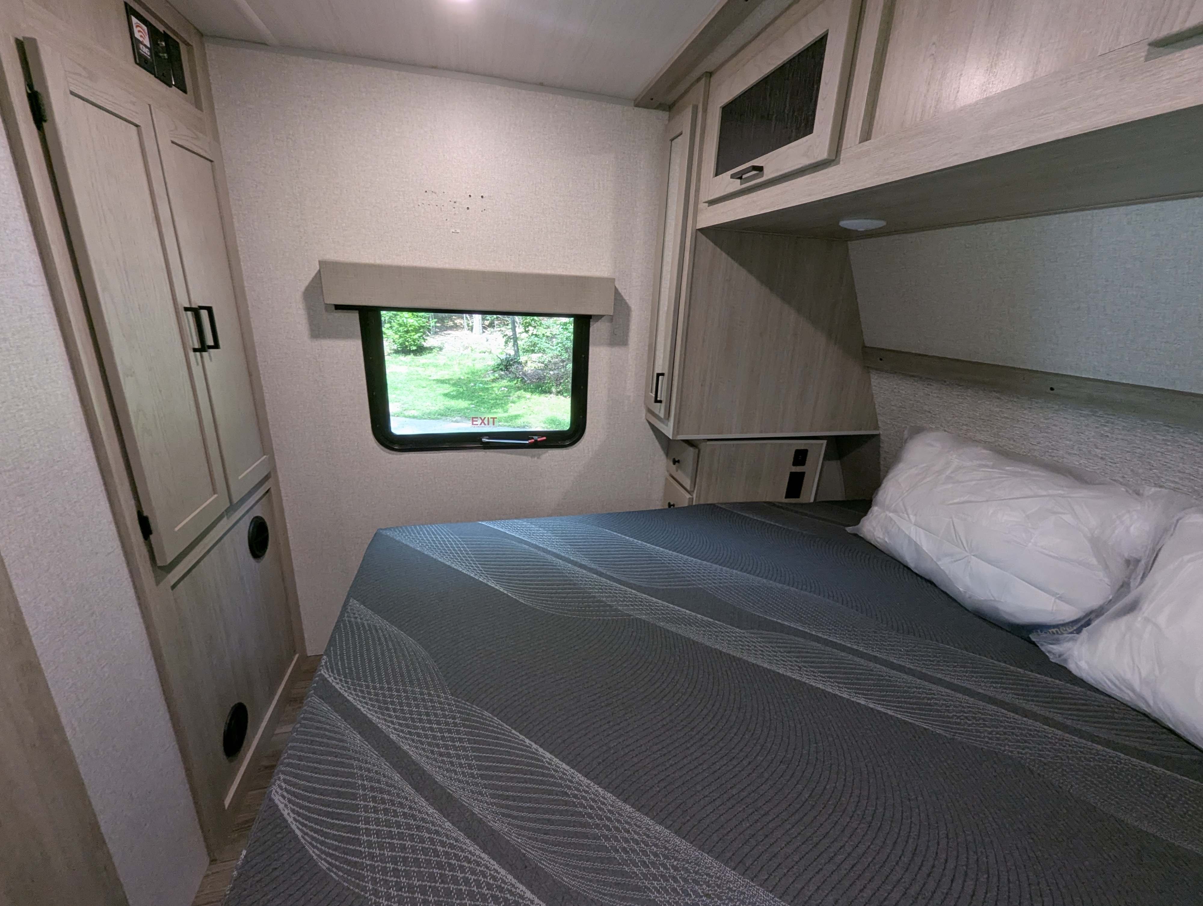 An RV rental bedroom with a gray bed, window overlooking nature, and functional light-colored cabinets and storage.. Forest River INC. Alta 2022