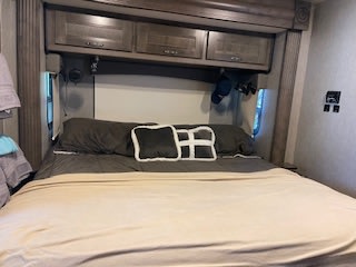 This inviting RV rental bedroom features a spacious bed with pillows, overhead cabinets, and side lights, ready for your adventure.. Nexus RV Maybach 2020