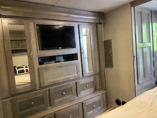 Inside this modern RV rental bedroom, a large wooden dresser with a mounted TV & mirrors offers extensive storage.. Nexus RV Maybach 2020