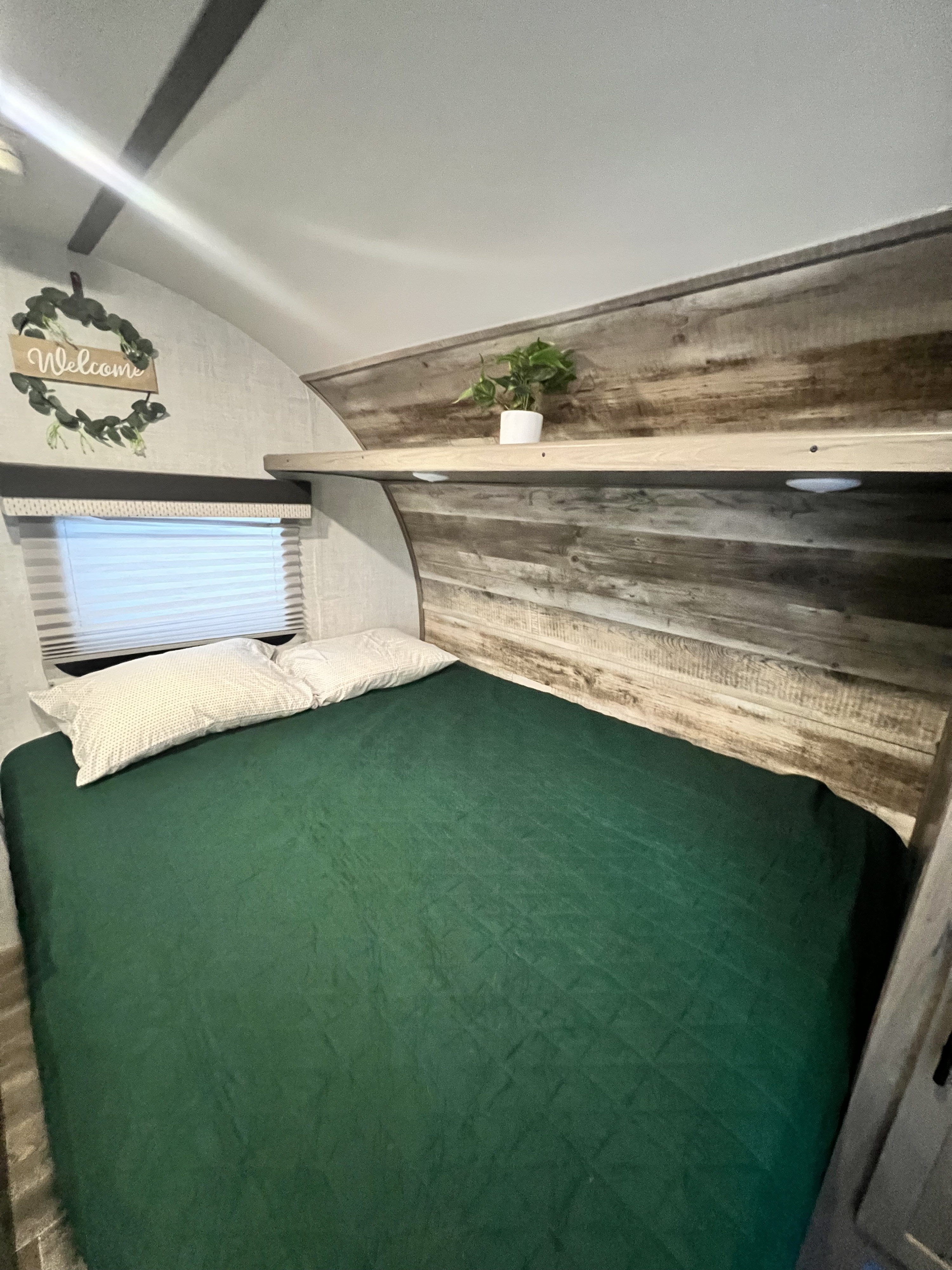 Cozy RV rental bedroom with a green bed, wood headboard, and "Welcome" sign. Ideal for your next journey.. Gulf Stream Ameri-Lite Super Lite 2021