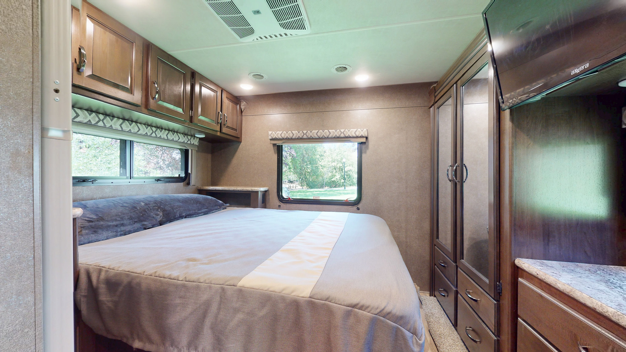 Comfortable RV rental bedroom with a queen bed, overhead cabinets, TV, and wardrobe, offering a restful travel space.. Thor Four Winds 2020