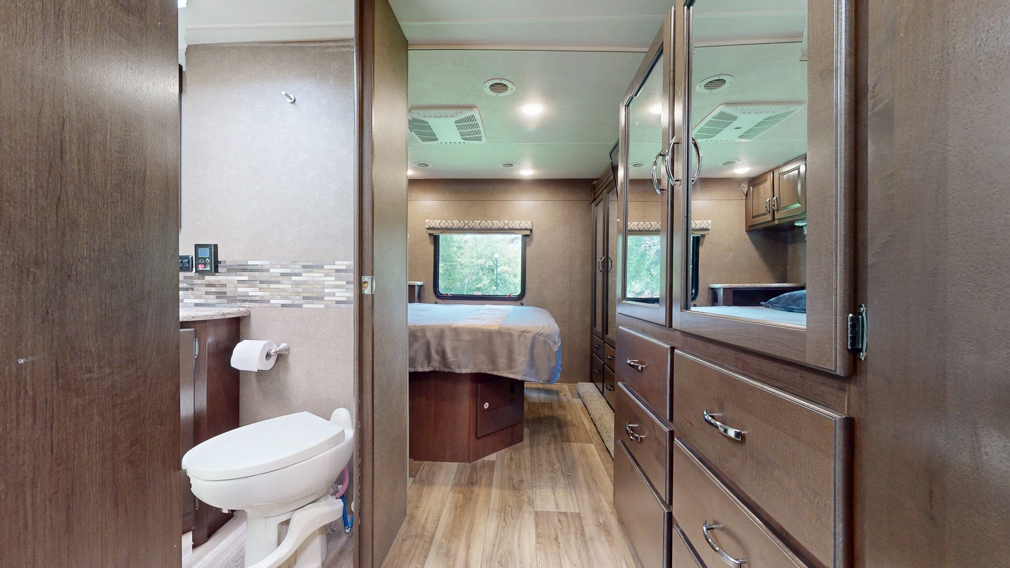 RV rental interior: bedroom with comfy bed and mirrored storage, adjacent to a compact bathroom with a toilet and sink area.. Thor Four Winds 2020