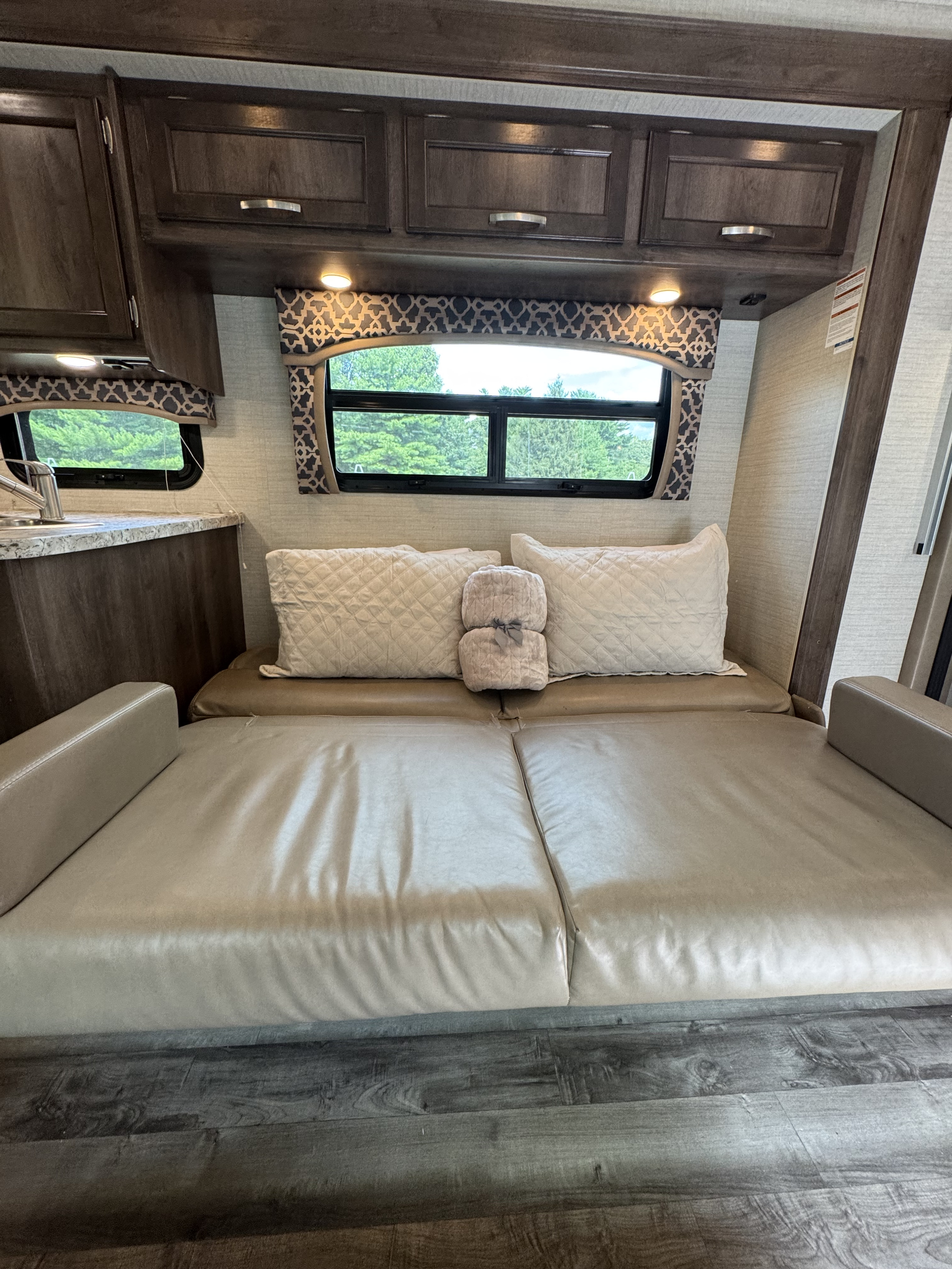 Cozy RV rental interior featuring a convertible sofa-bed, overhead cabinets, and large windows with outdoor views.. Jayco Alante 2019