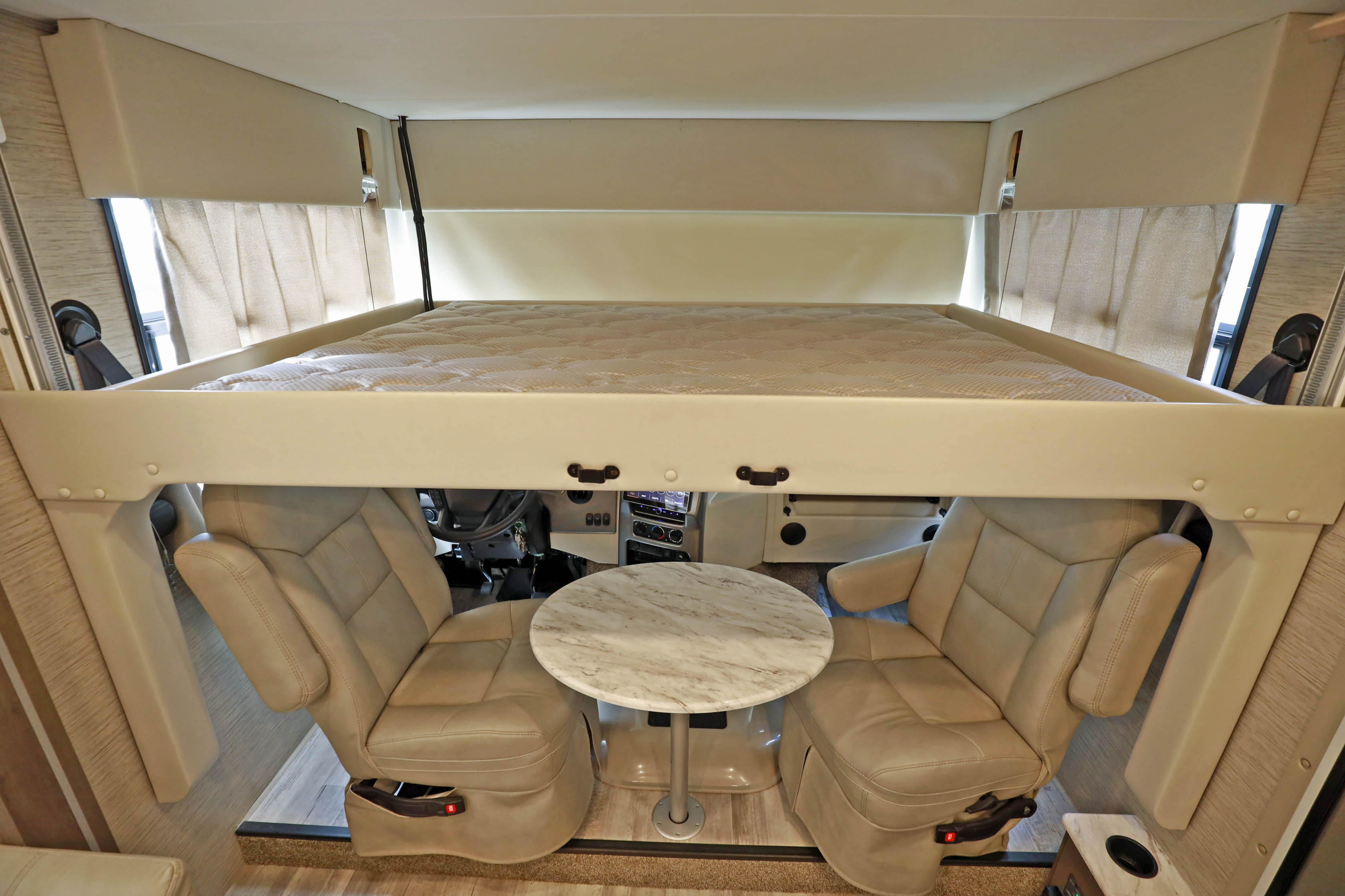Spacious RV rental interior showing a drop-down bed, swivel captain's chairs, and a small table.. Classe A 31 pieds avec extensions 2021