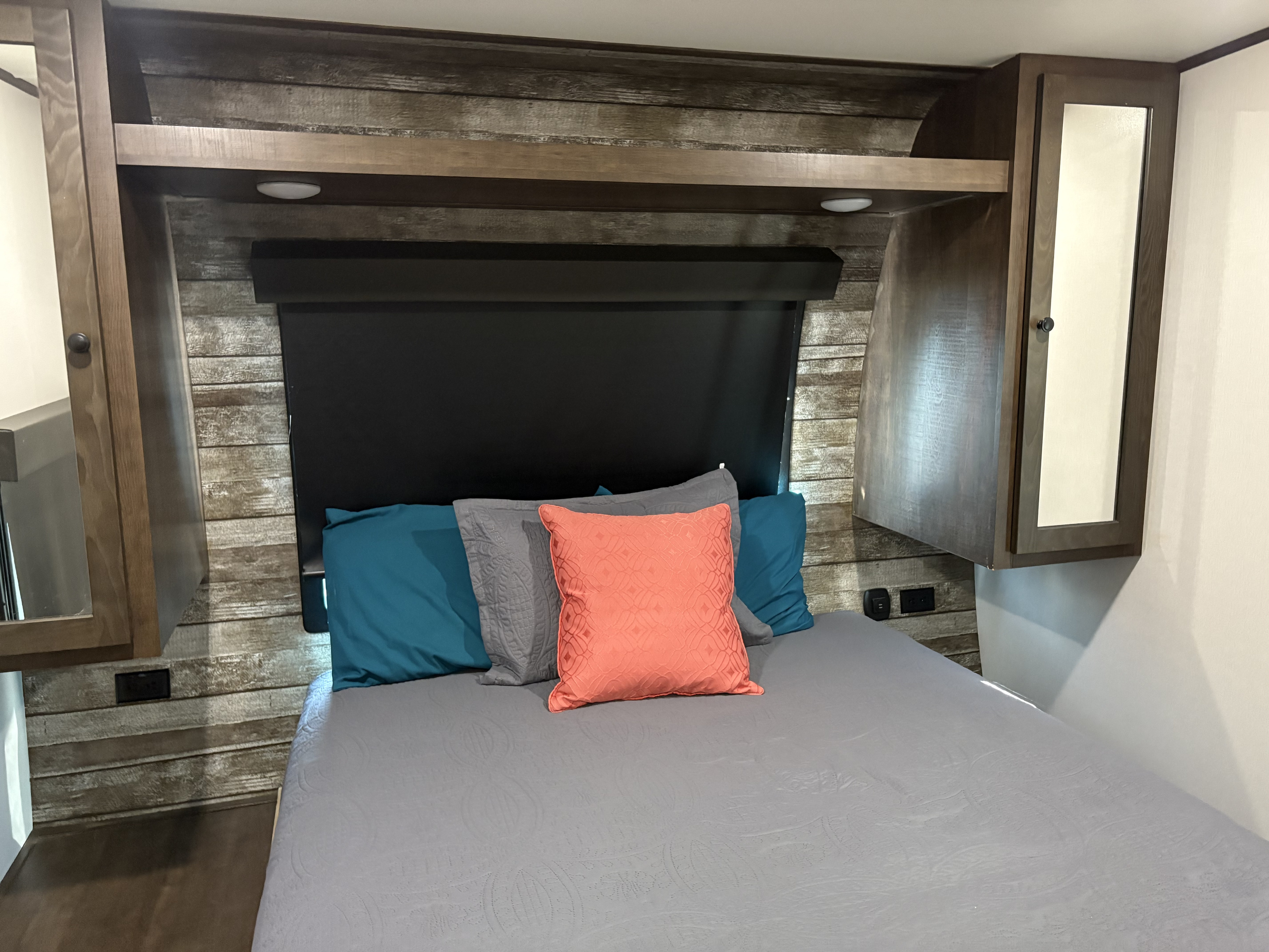RV rental bedroom with comfortable bed, teal and coral pillows, rustic wood-look walls, and built-in storage cabinets.. Forest River Hyperlight 2021