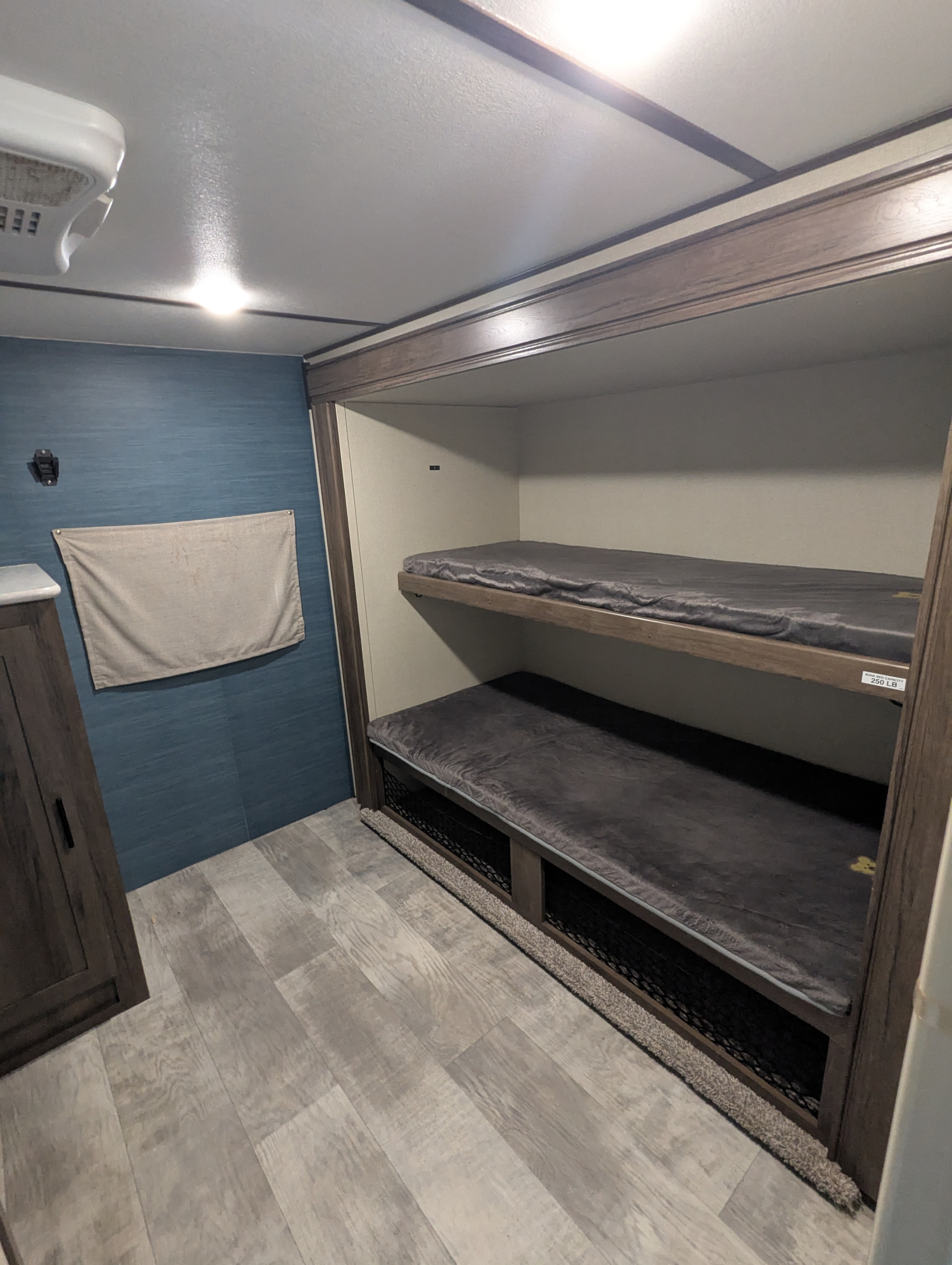 RV rental bunkhouse interior, showcasing two bunk beds with grey bedding, a blue accent wall, and wood-look floor.. PrimeTime Tracer 2020