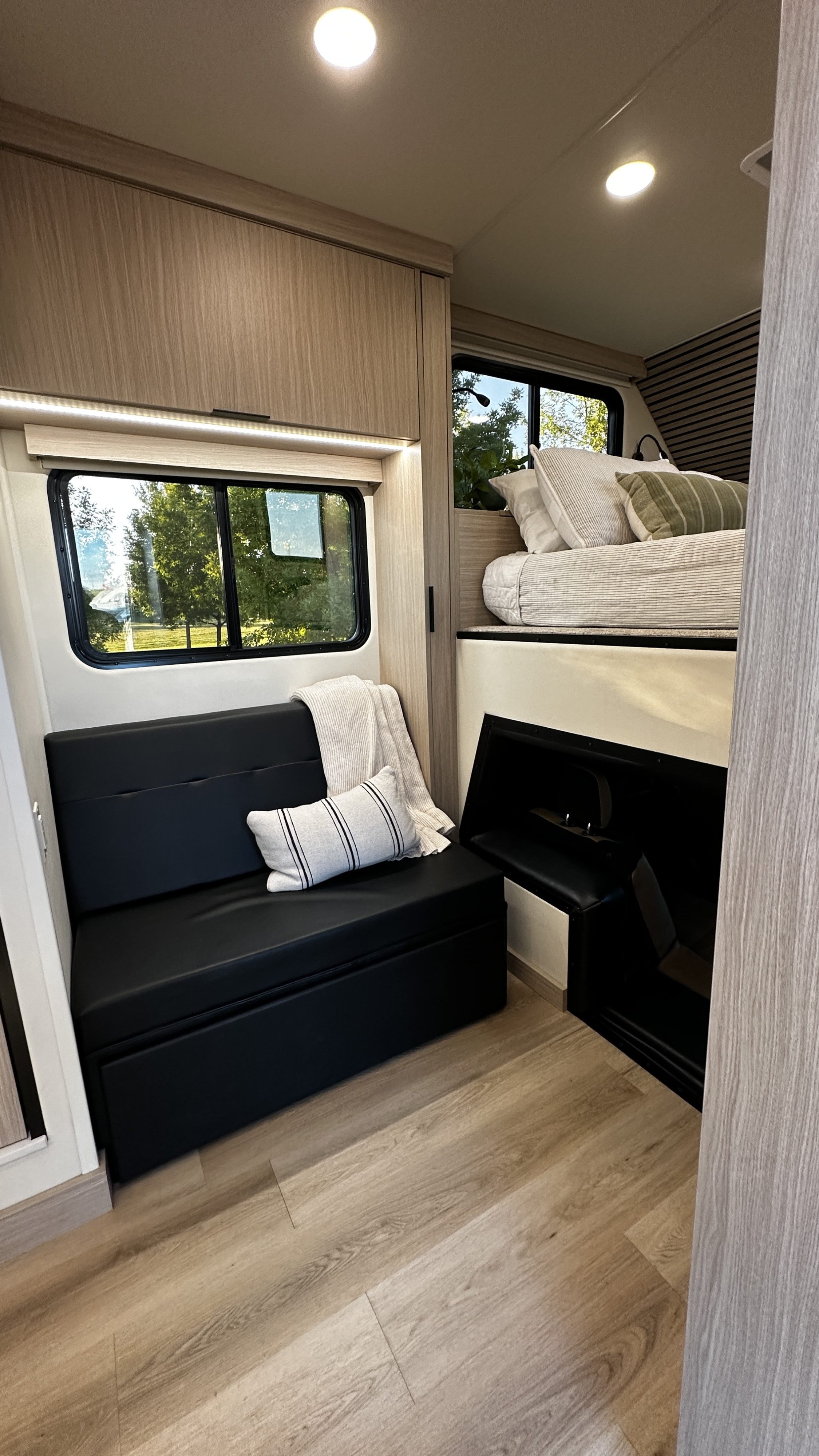 RV rental with a modern interior: comfy bed, black bench seating, window, and clever storage solutions.. iRoam Coaches The Roamer 2024