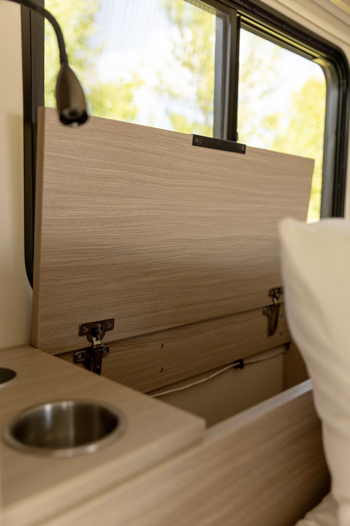 RV rental interior: Open wood panel reveals functional storage and cup holders, near a window for convenience.. iRoam Coaches The Roamer 2024