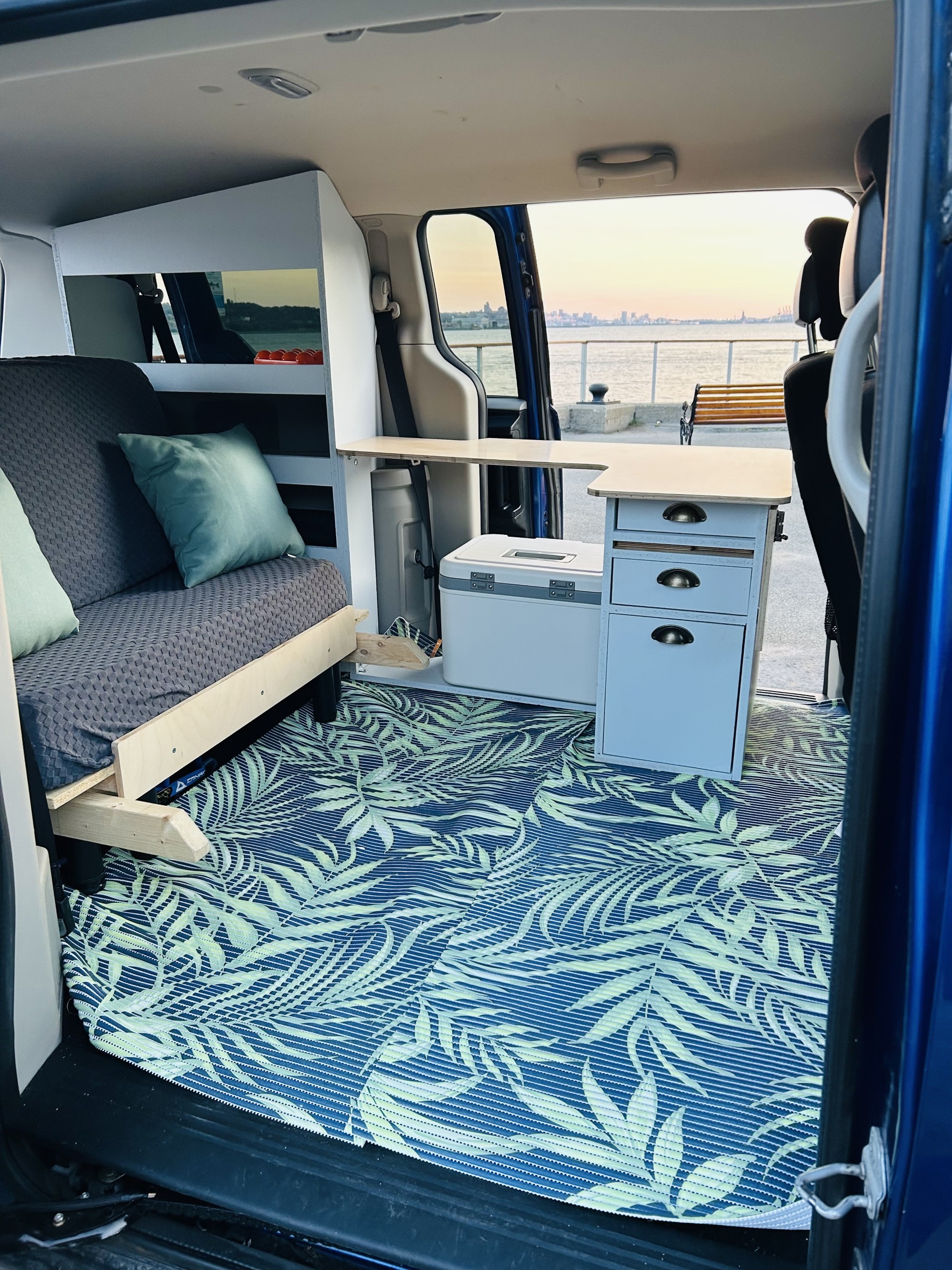 RV rental: Van conversion interior with sofa bed, modular kitchen unit, tropical floor mat, and waterfront city view at sunset.. Dodge Grand Caravan SE 2013