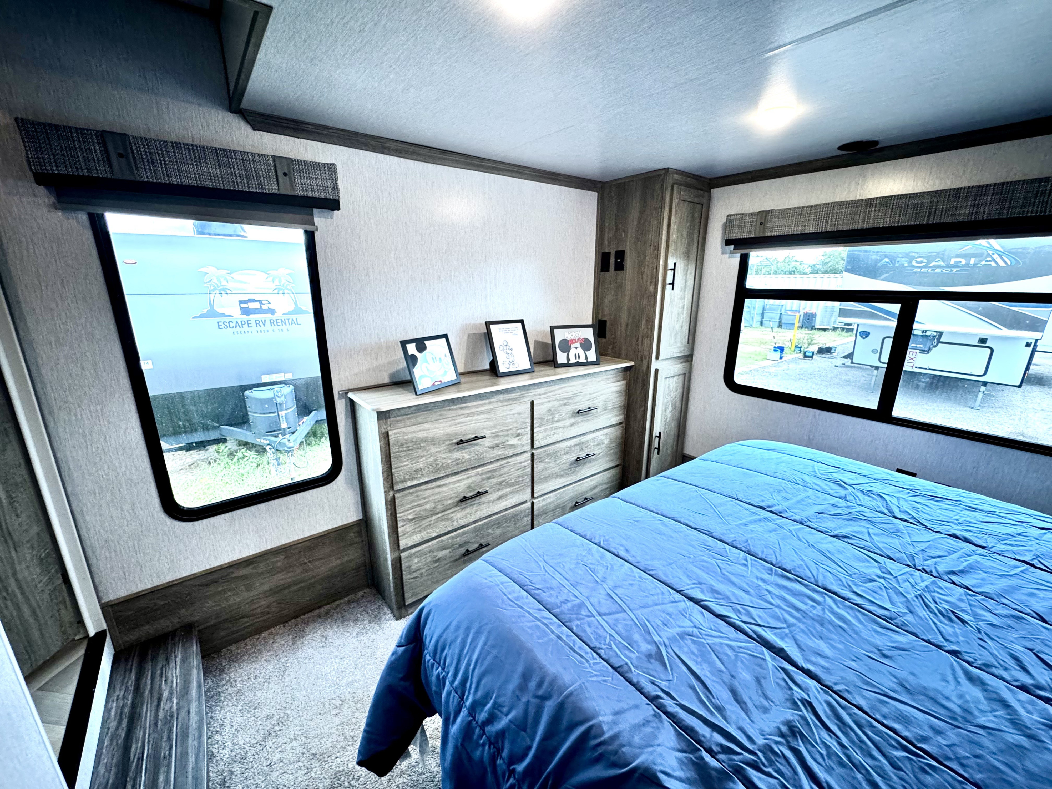 Cozy RV rental bedroom with a blue bed, dresser, and views outside. Modern and inviting interior.. Forest River Wildwood Heritage Glenn 2024