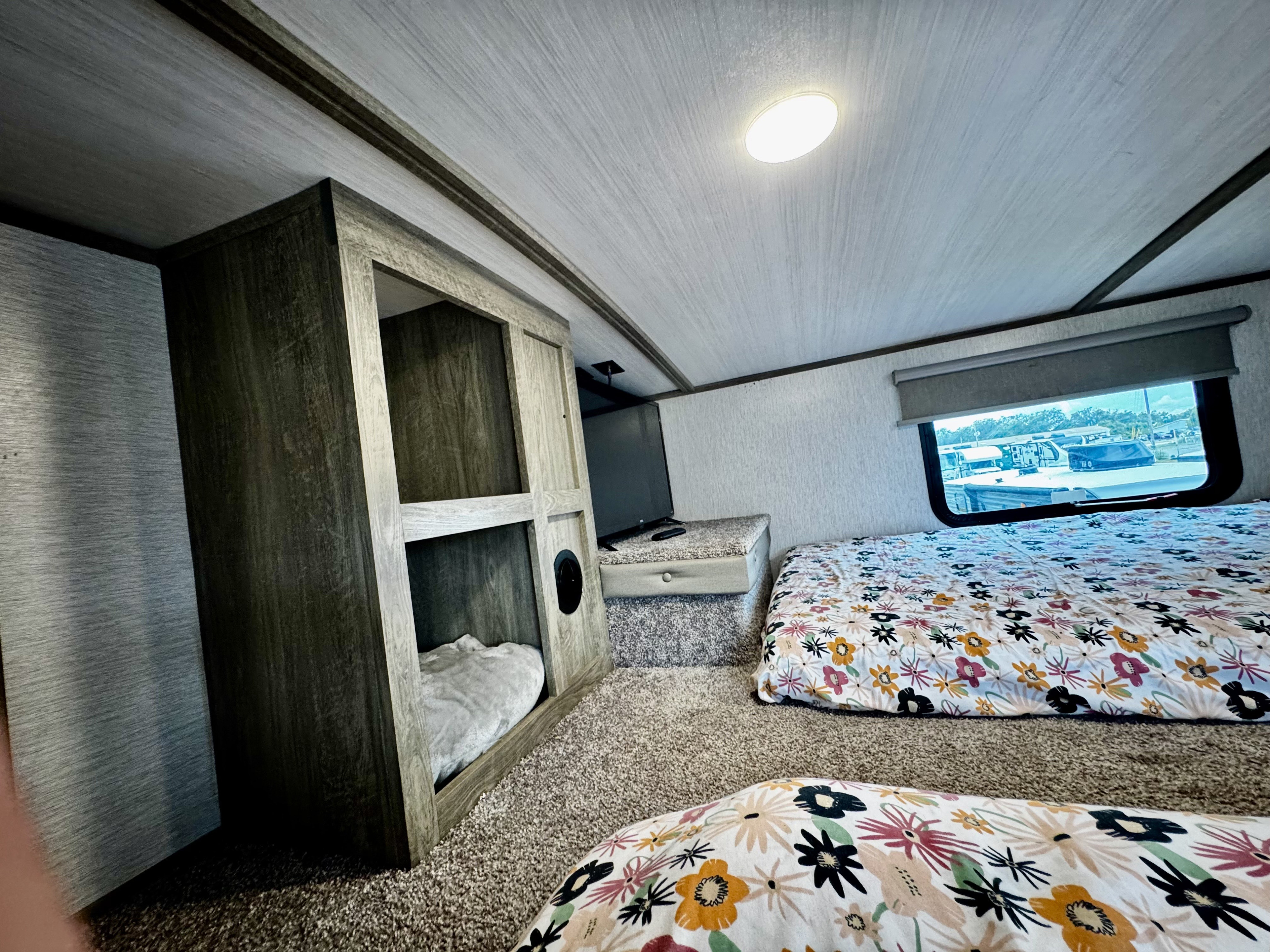 Comfortable RV rental sleeping area with floral beds, built-in bunk, TV, and window view, ideal for travel.. Forest River Wildwood Heritage Glenn 2024