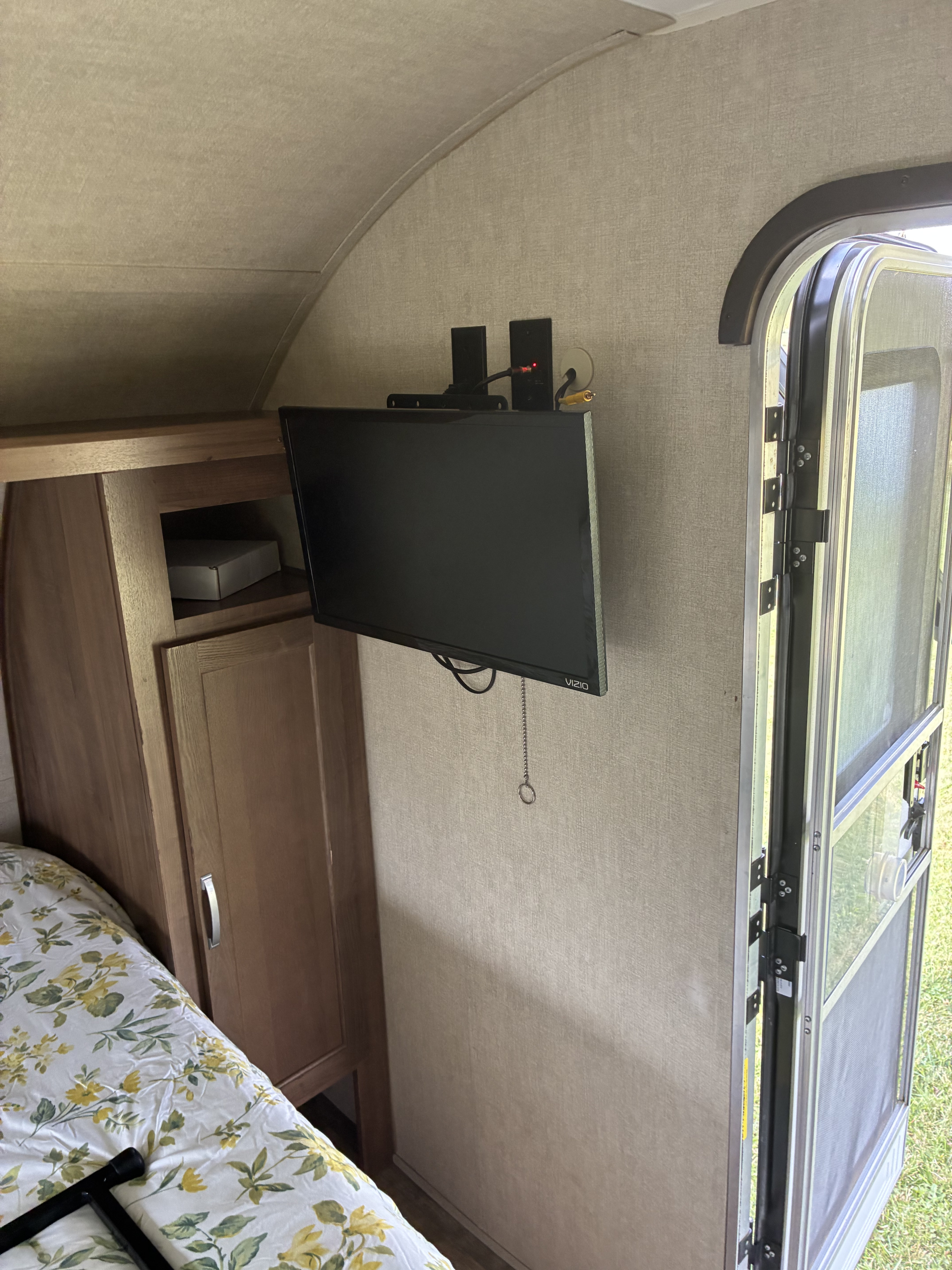 Inside a cozy RV rental bedroom featuring a mounted TV, storage cabinet, and an open screen door to the outside.. Gulf Stream Ameri-Lite 2019