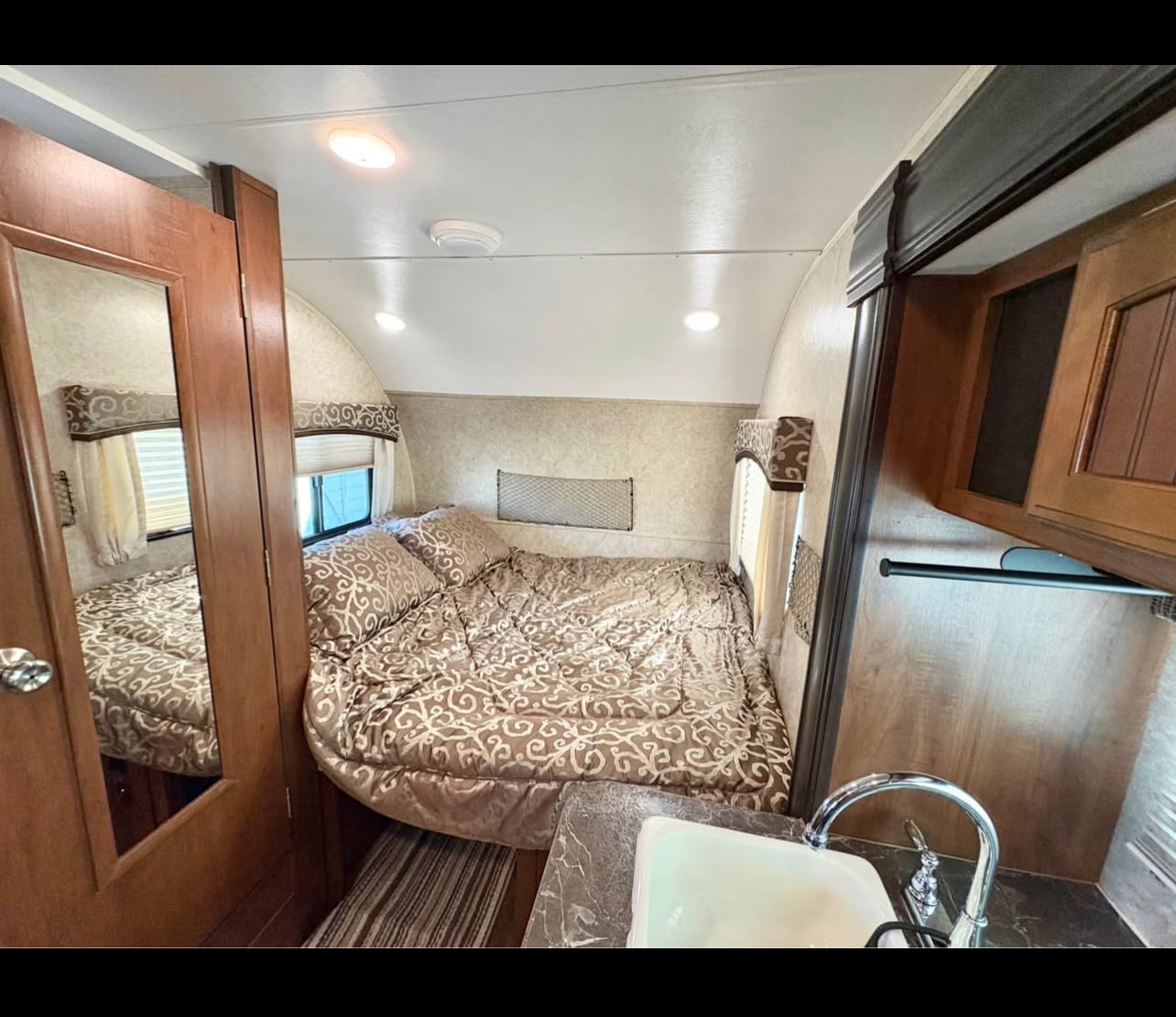 RV rental interior showcasing a comfortable bed, compact kitchen sink area, and warm wood details.. Jayco Hummingbird Baja Edition 2018