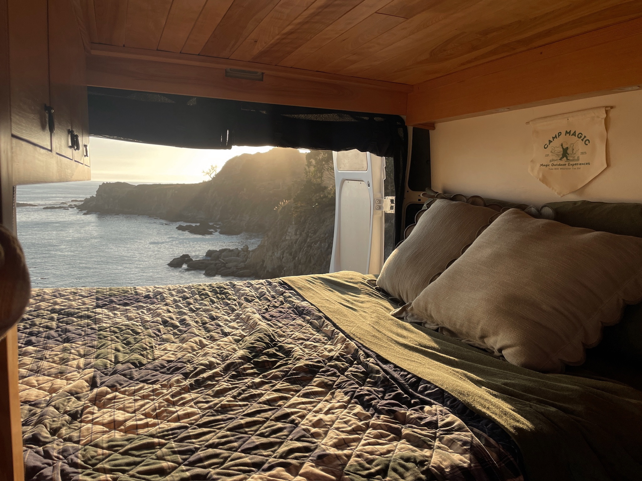 Stunning RV rental view: cozy bed facing a golden ocean sunset from inside a camper van. Perfect for travel.. Dodge 1500 2018