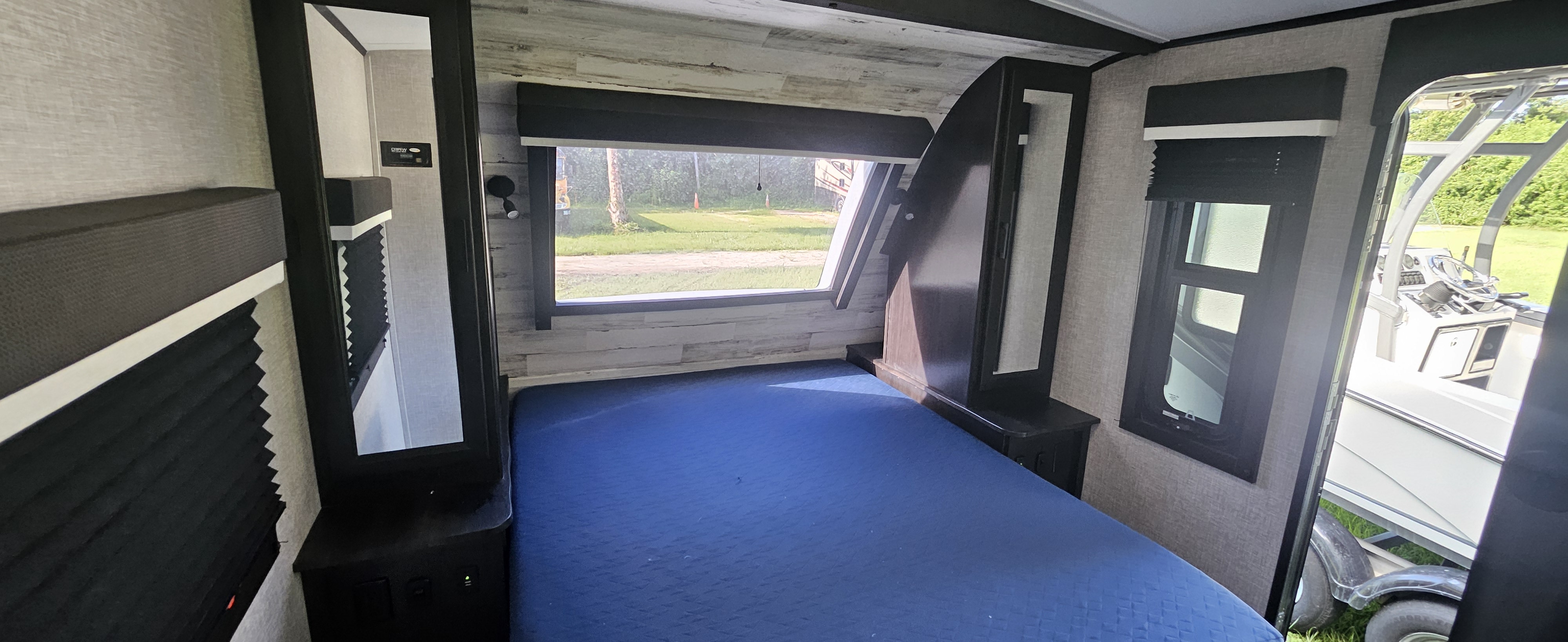 Inside an RV rental: a blue bed, wall storage, and windows revealing an outdoor scene with trees and a boat.. Jayco White Hawk 2022
