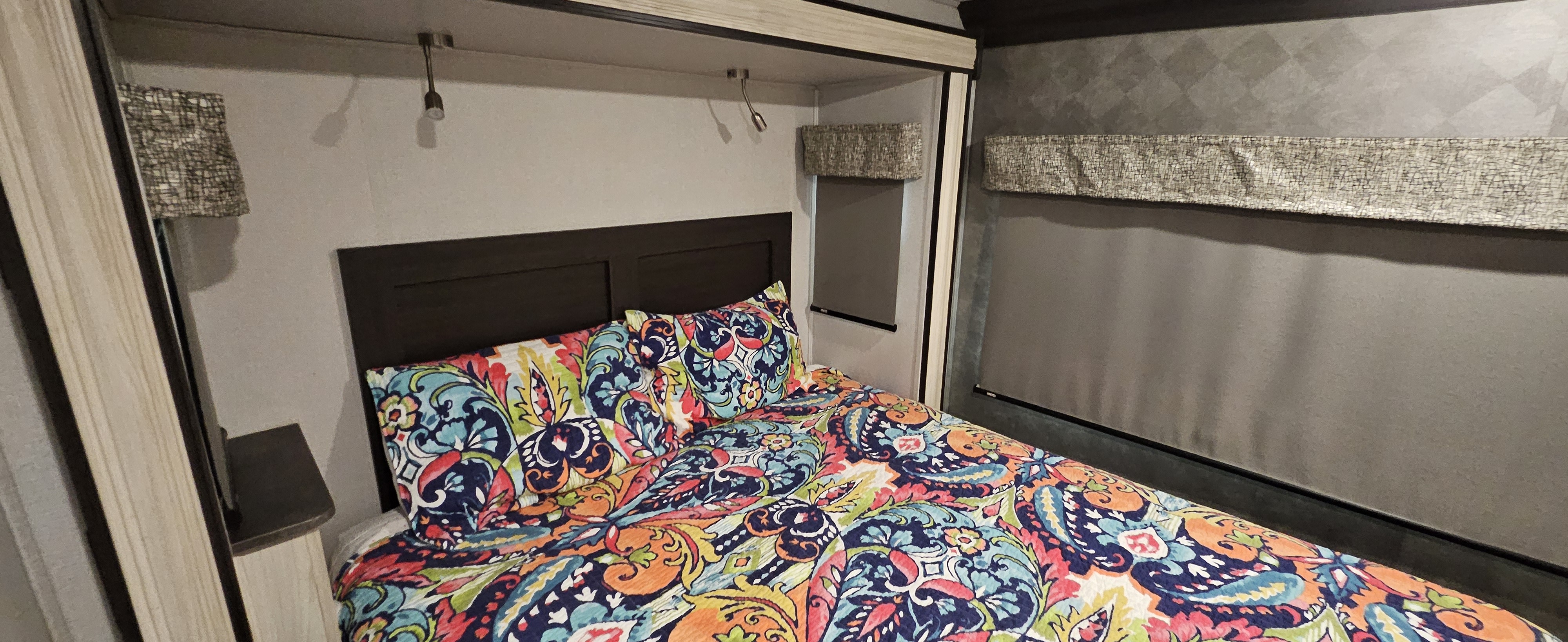 A vibrant rv rental bedroom with a colorful quilt, dark headboard, two reading lights, and window blinds.. Forester Classic 2021