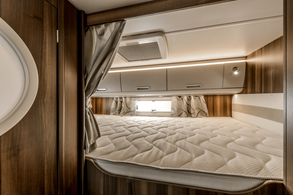 Cozy RV rental sleeping area featuring a quilted mattress, ambient lighting, storage cabinets, and privacy curtains.. Other Superbrig 687 TC 2025