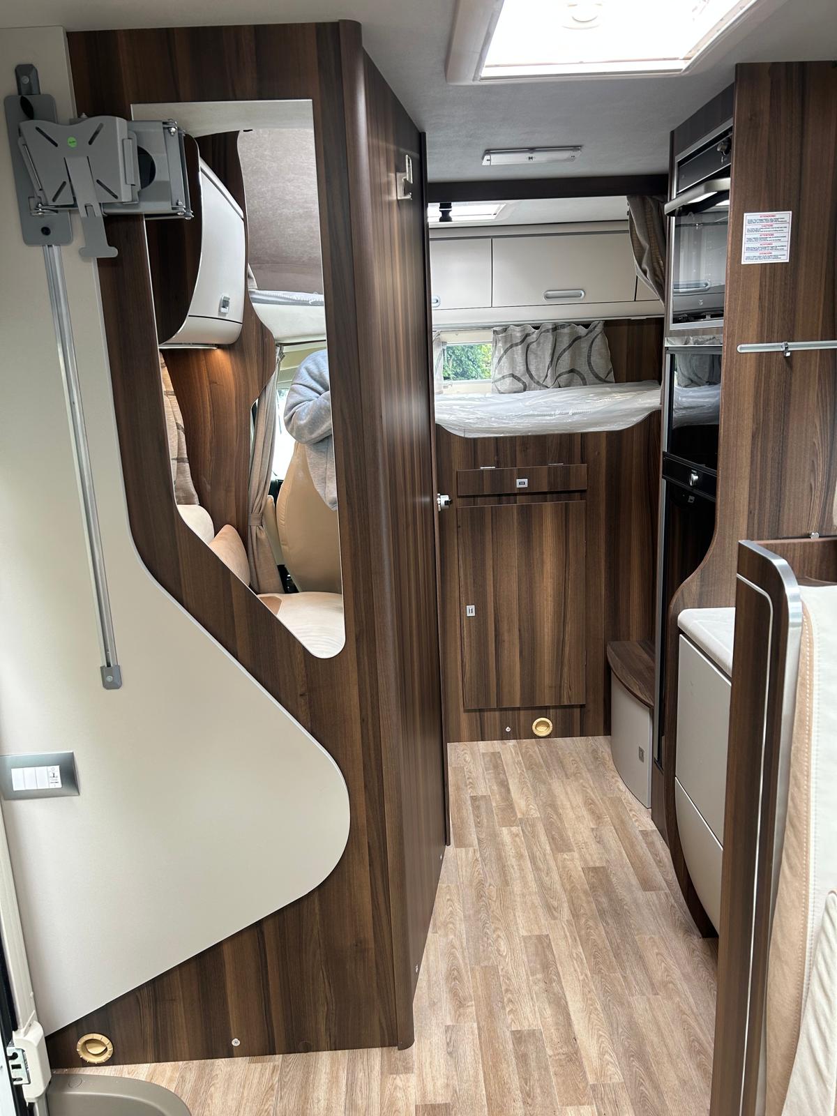 Modern RV rental interior with compact living space: kitchen, bed, wood floor, and TV mount. Ideal for travel.. Other Superbrig 687 TC 2025