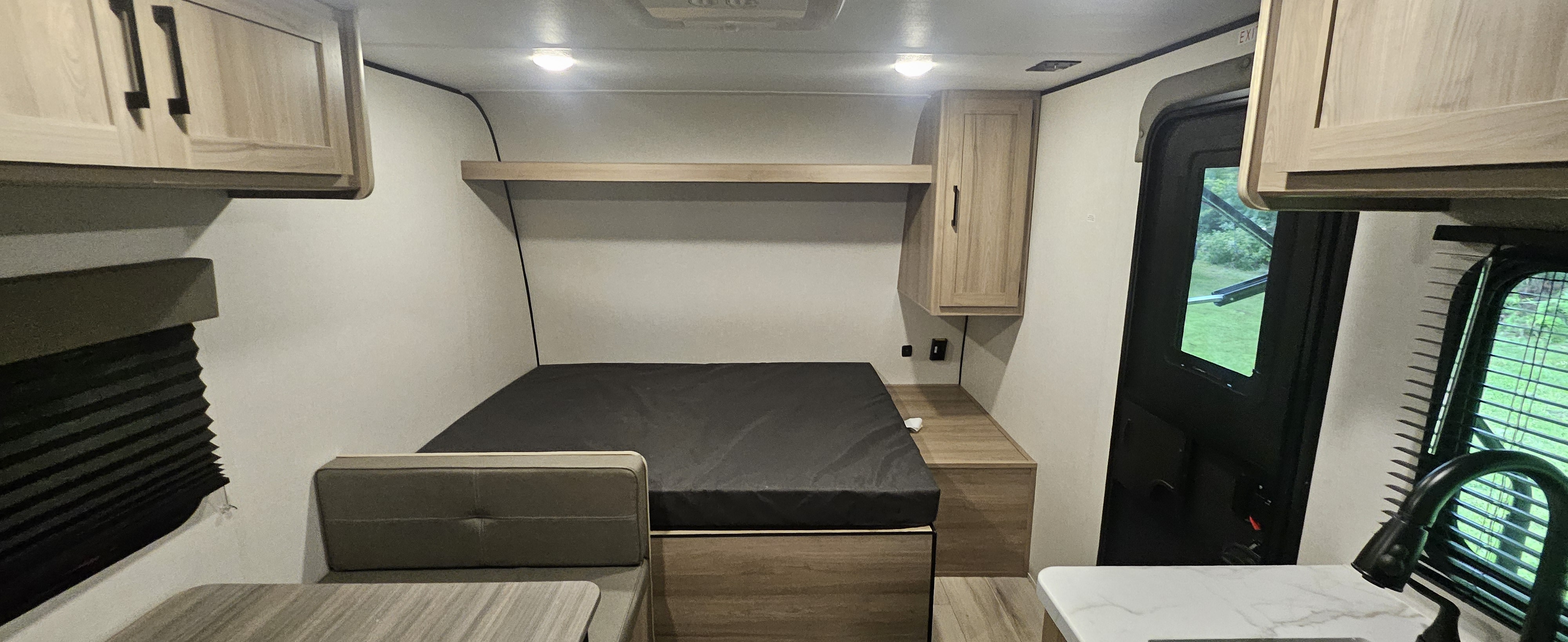 RV rental interior features a compact bed, dinette, overhead cabinets, and a partial kitchen area, offering comfort and convenience.. coleman Keystone Light 2025