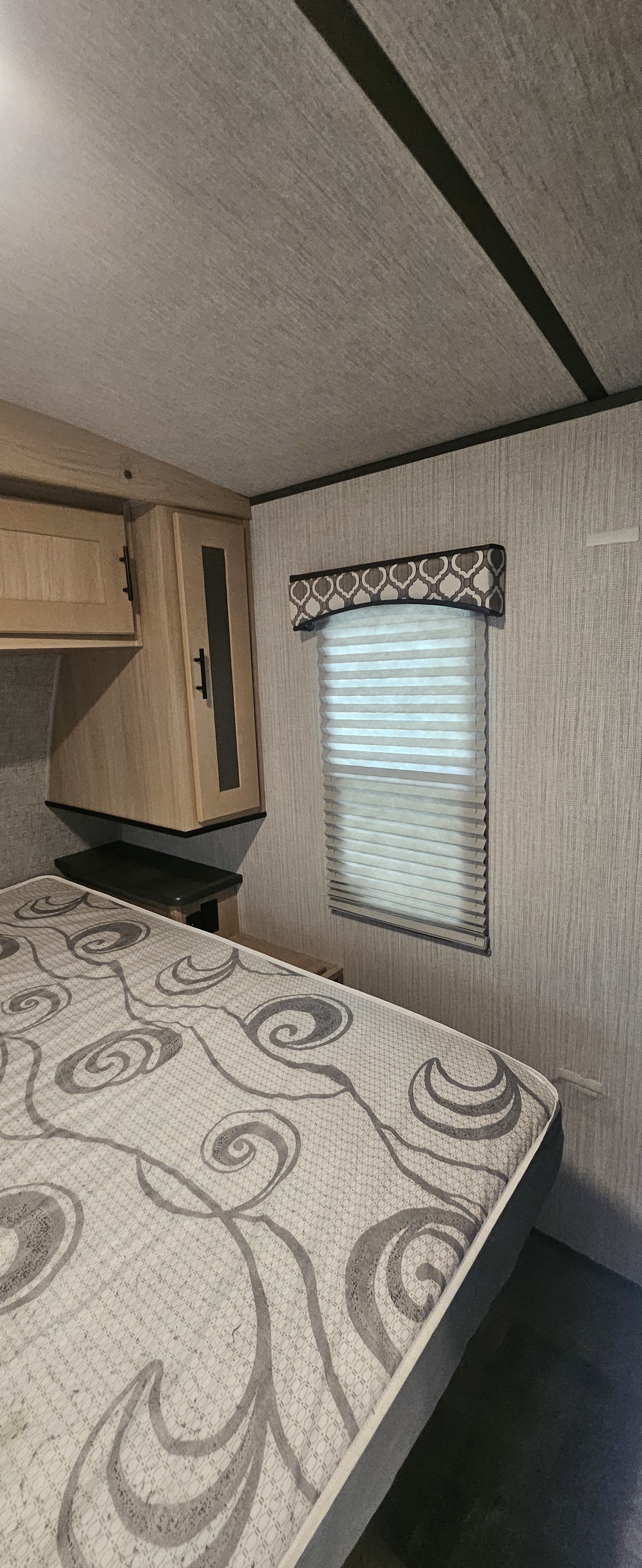 Cozy RV rental bedroom features a patterned mattress, wood cabinets, and a window with blinds.. Cruiser RV Radiance Ultra Lite 2020