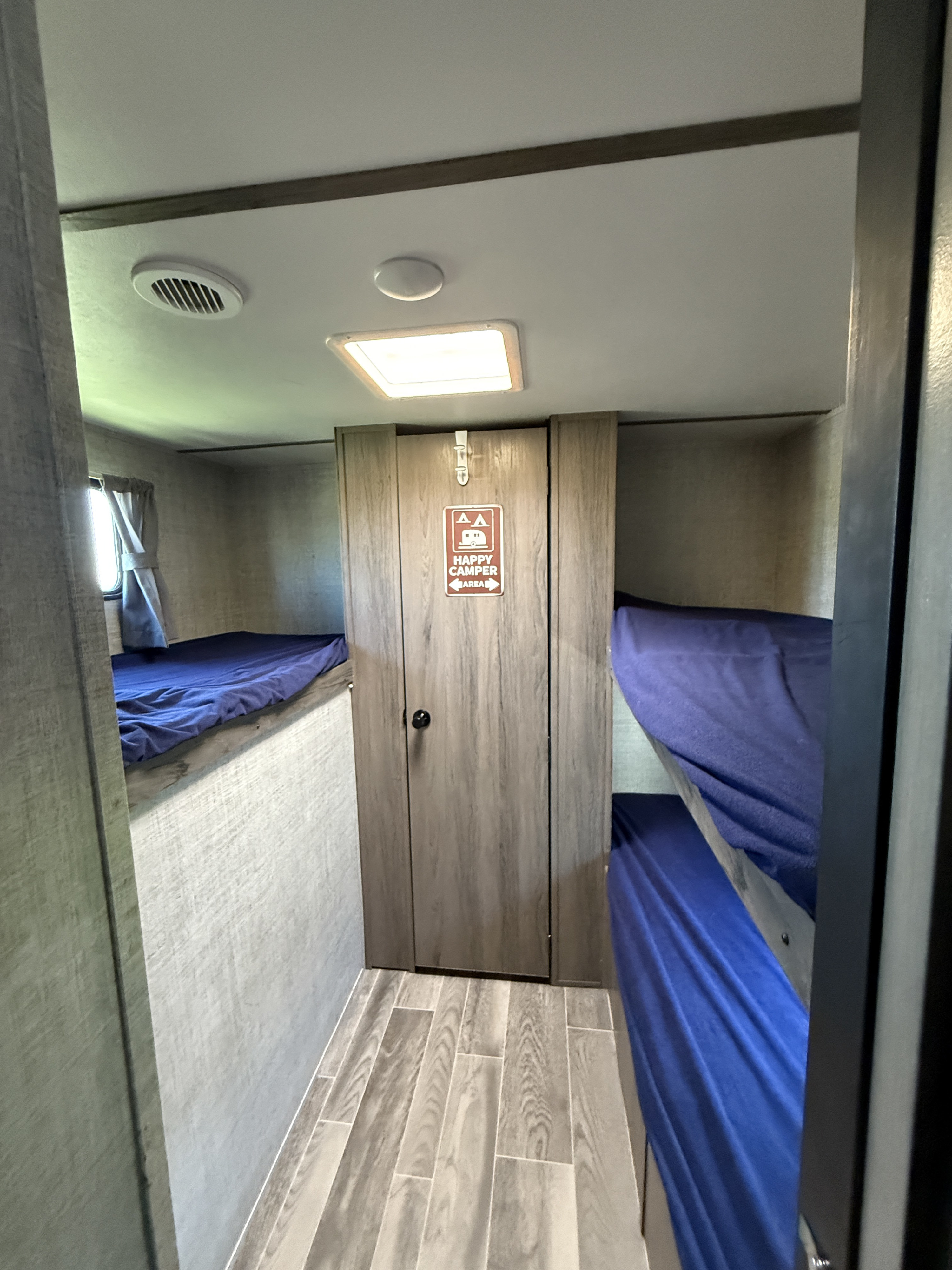 An rv rental's bunk bed area with blue sheets, a "Happy Camper Area" sign on a central closet, and wood-look floors.. Gulf Stream Kingsport 2021