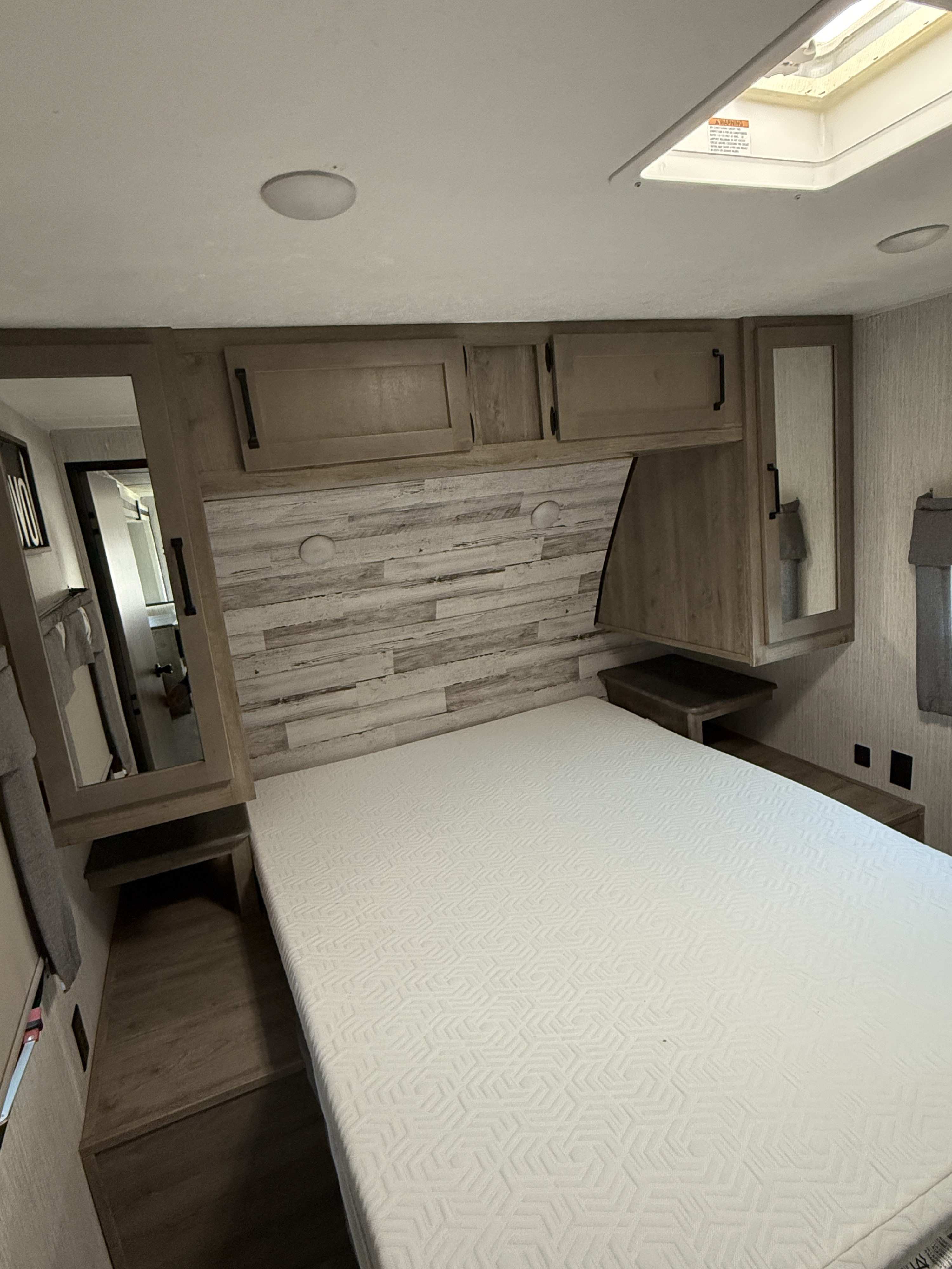 RV rental bedroom: a comfortable bed with a textured mattress, light wood-look paneling, overhead cabinets, and a ceiling skylight.. Palomino Puma 2022