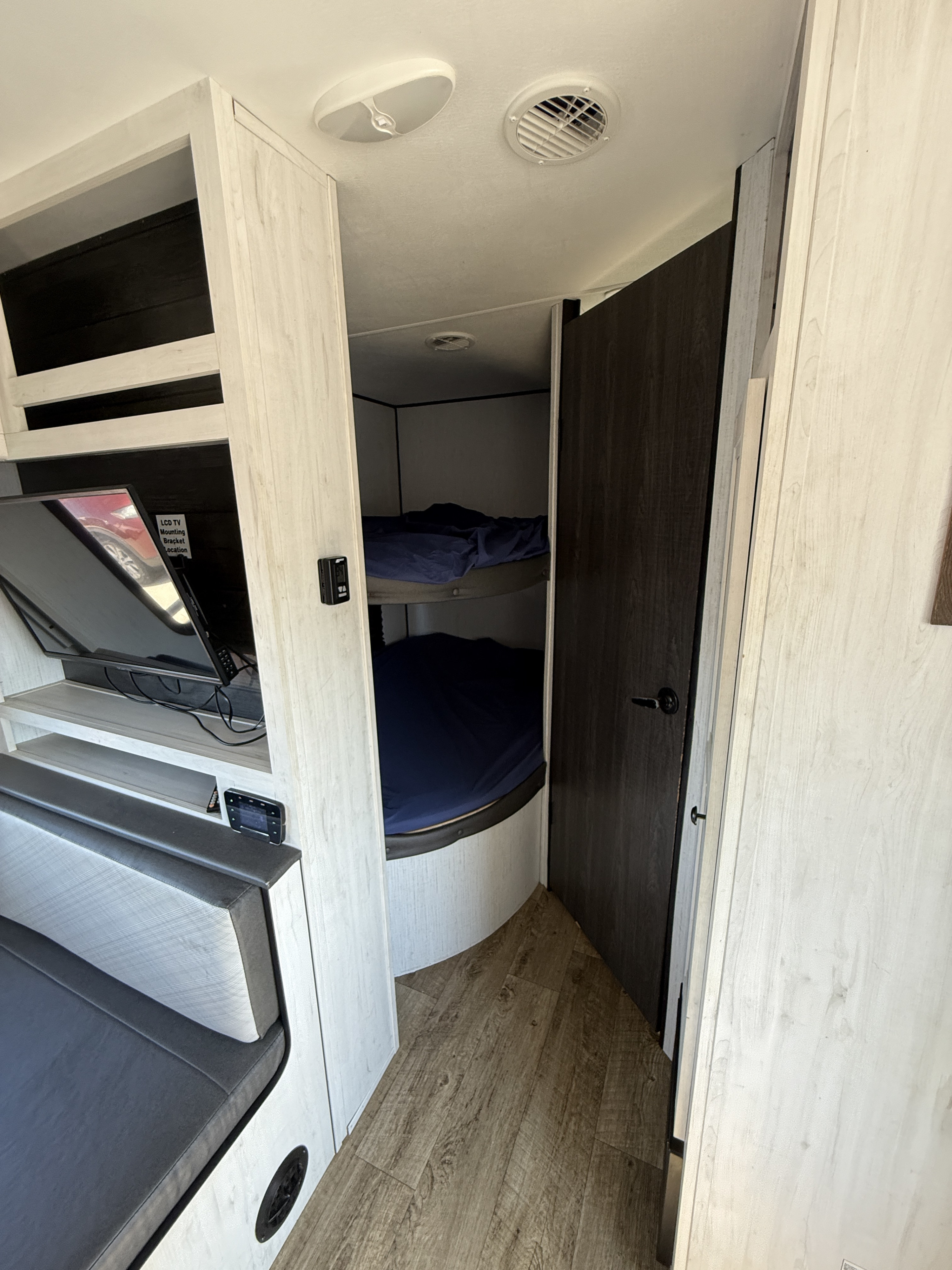 This RV rental interior features cozy bunk beds, a TV in the living space, and light wood grain cabinetry.. Heartland Trail Runner 2022