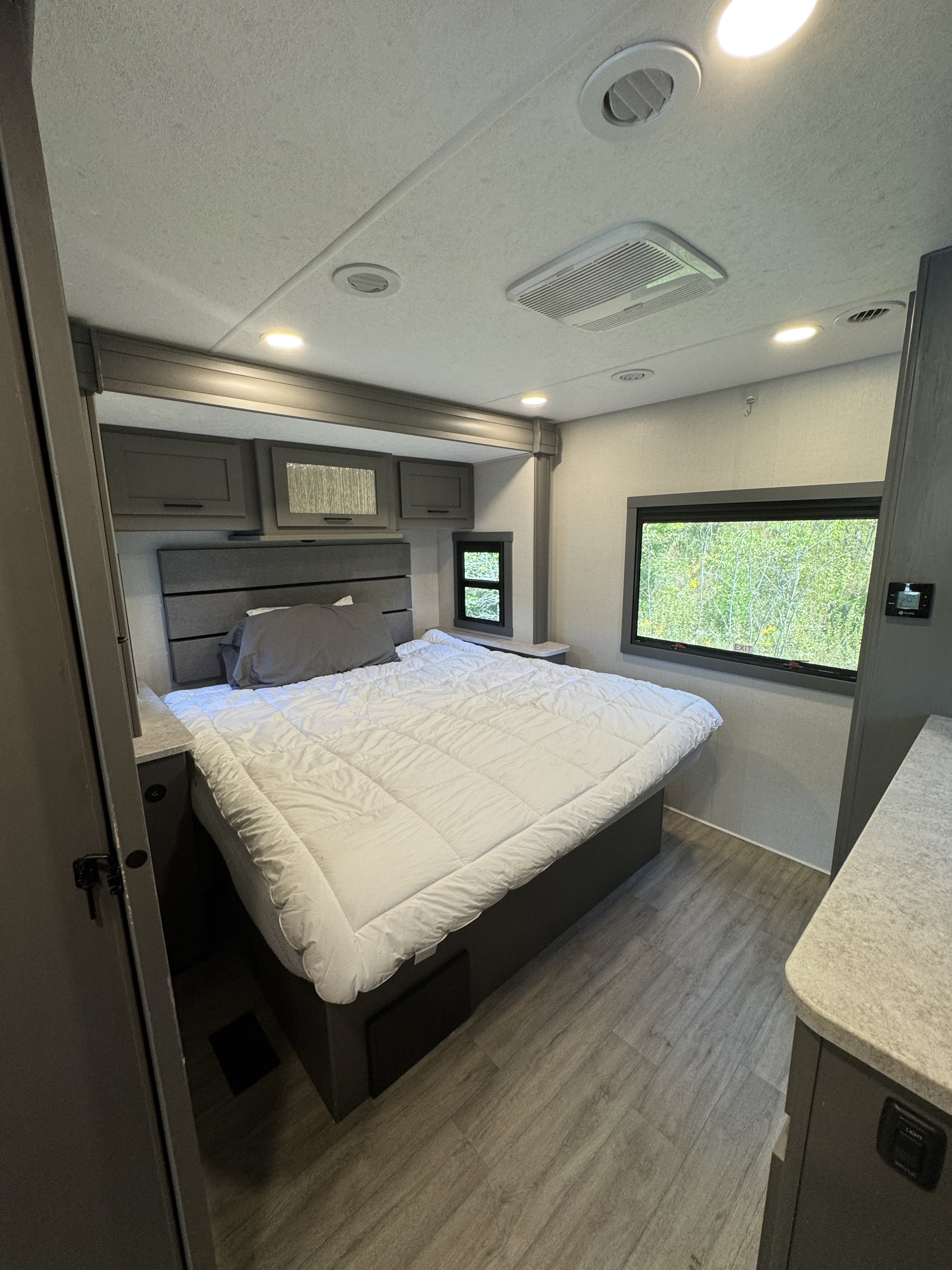Spacious, modern RV rental bedroom featuring a cozy bed, overhead cabinets, and large windows with nature views.. Coachmen Pursuit 2025