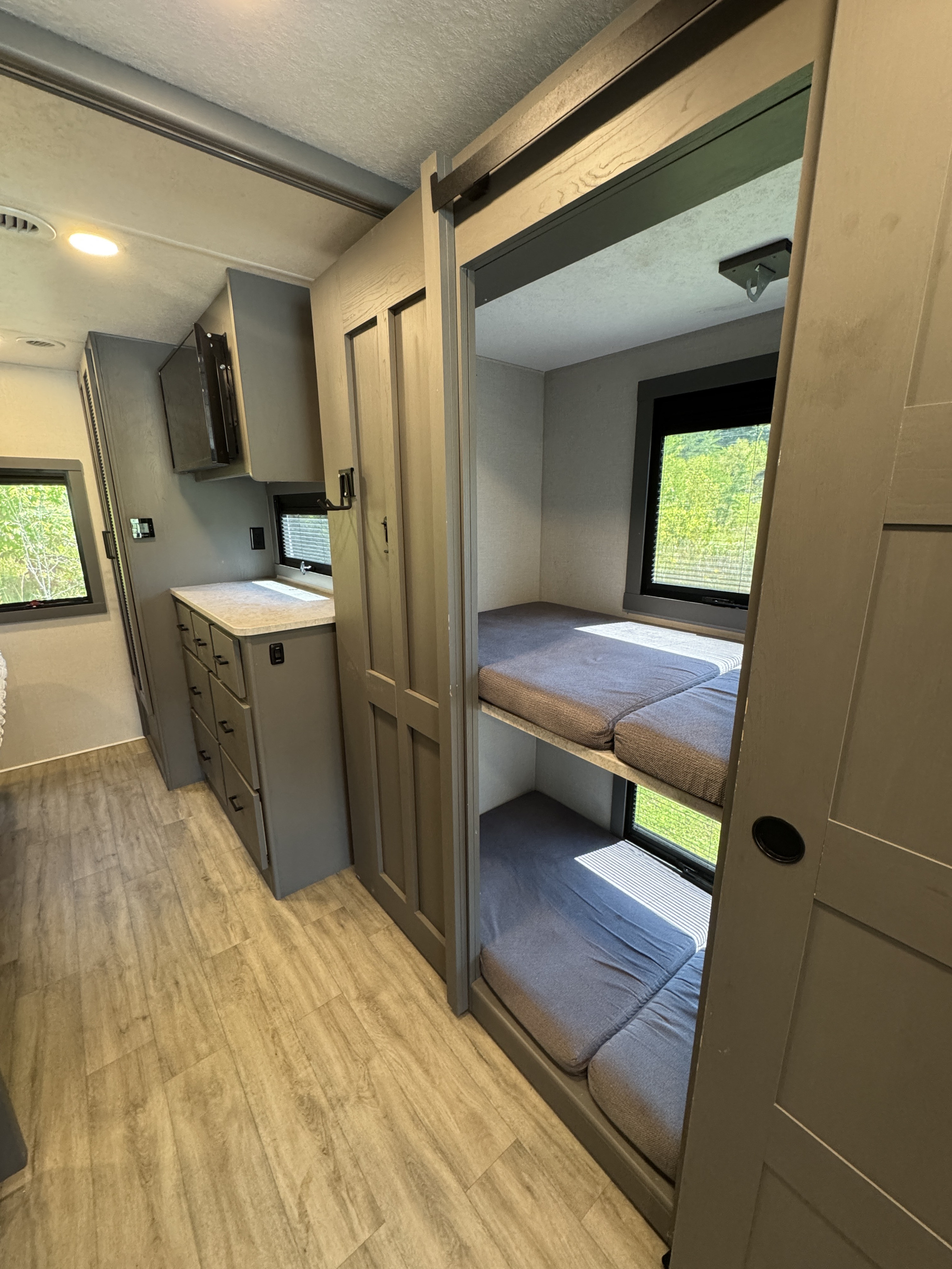 Modern gray RV rental interior: compact kitchen area, light wood-look flooring, and cozy bunk beds.. Coachmen Pursuit 2025