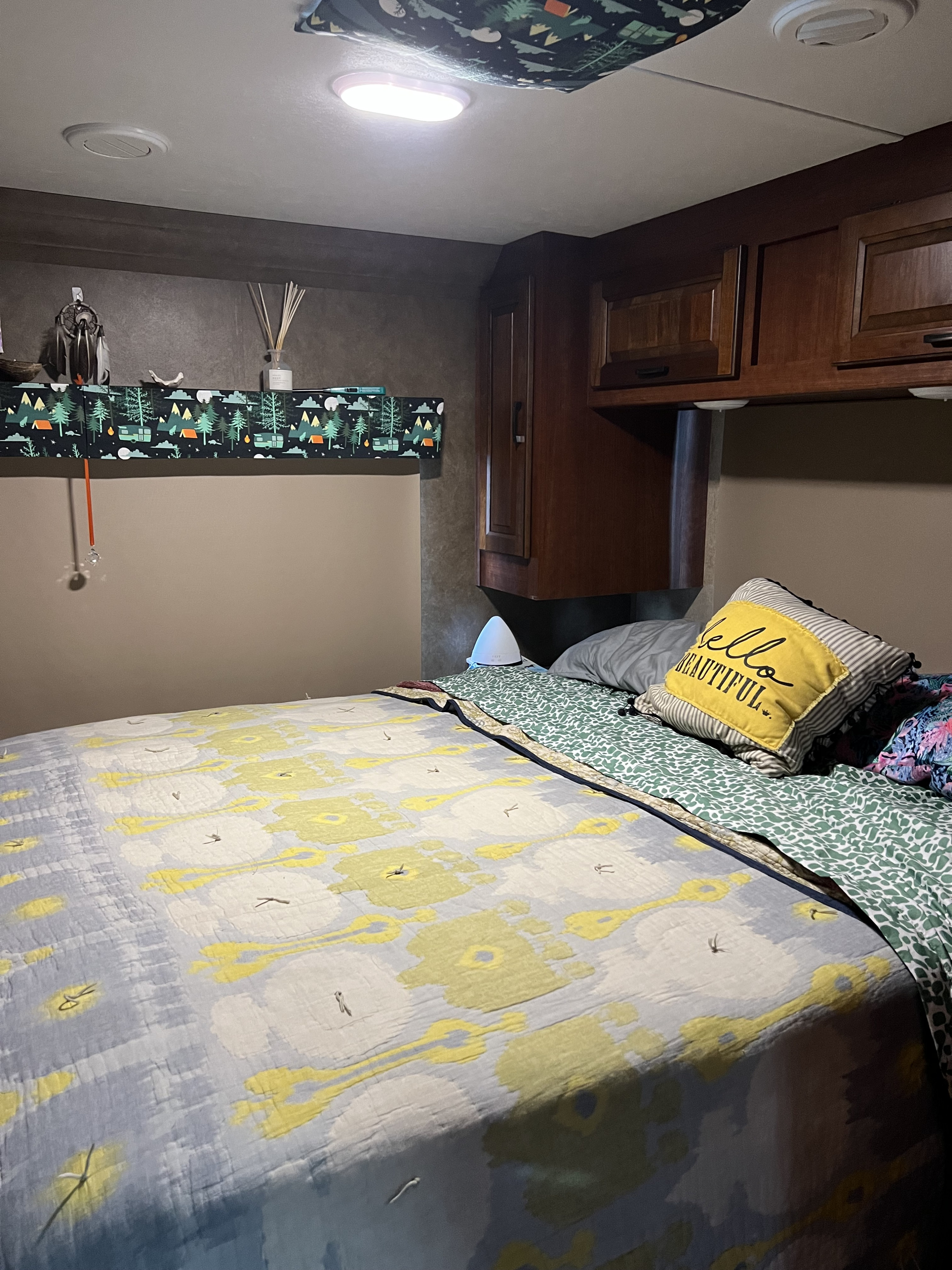 Cozy RV rental bedroom featuring patterned bedding, wooden overhead cabinets, and a decorative shelf, illuminated by ceiling lights.. Forest River Sunseeker LE 2017
