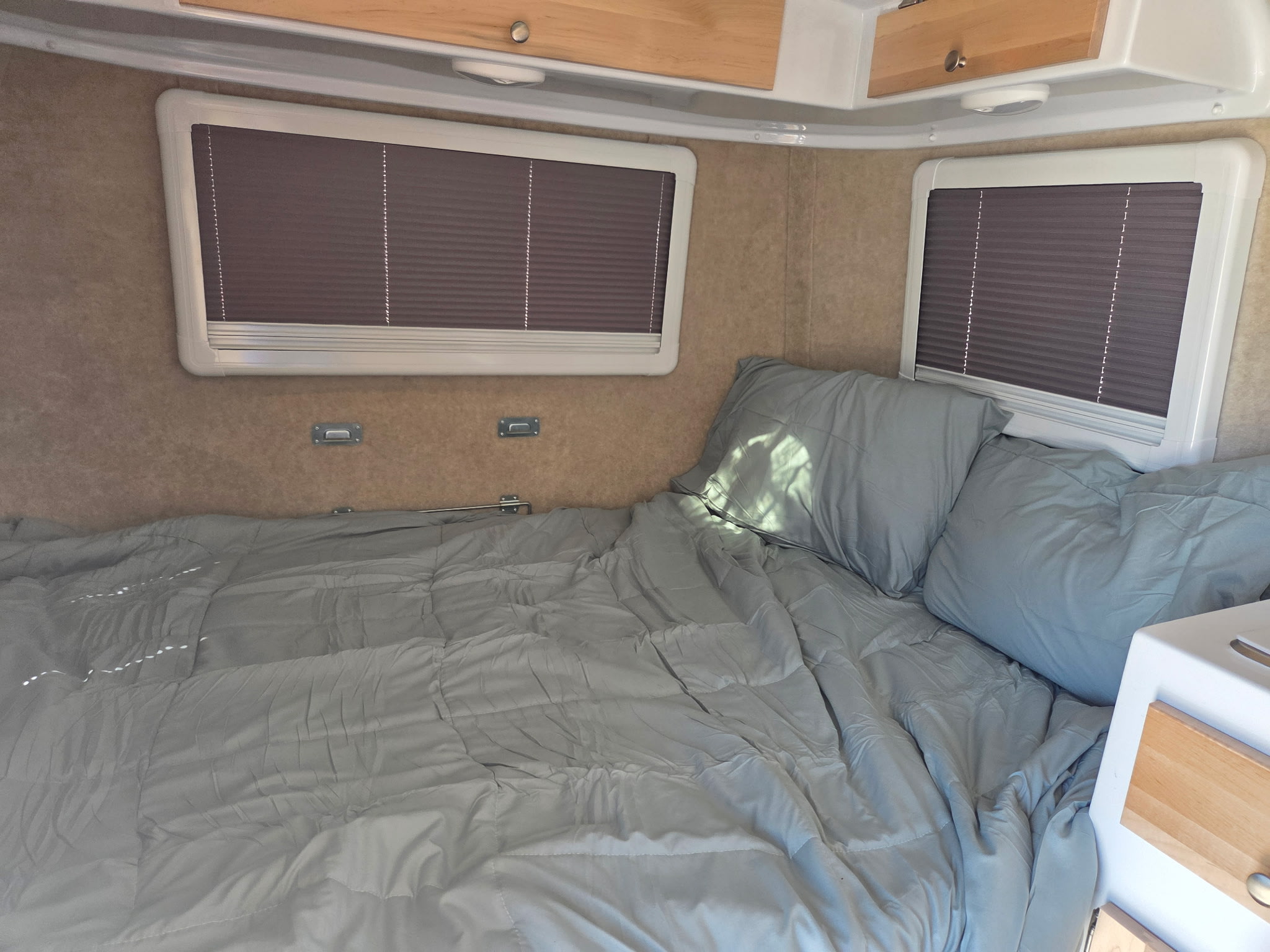 Cozy RV rental interior with a light grey bed, pillows, and windows with blinds, perfect for comfortable travel.. SCAMP SCAMP13 2025