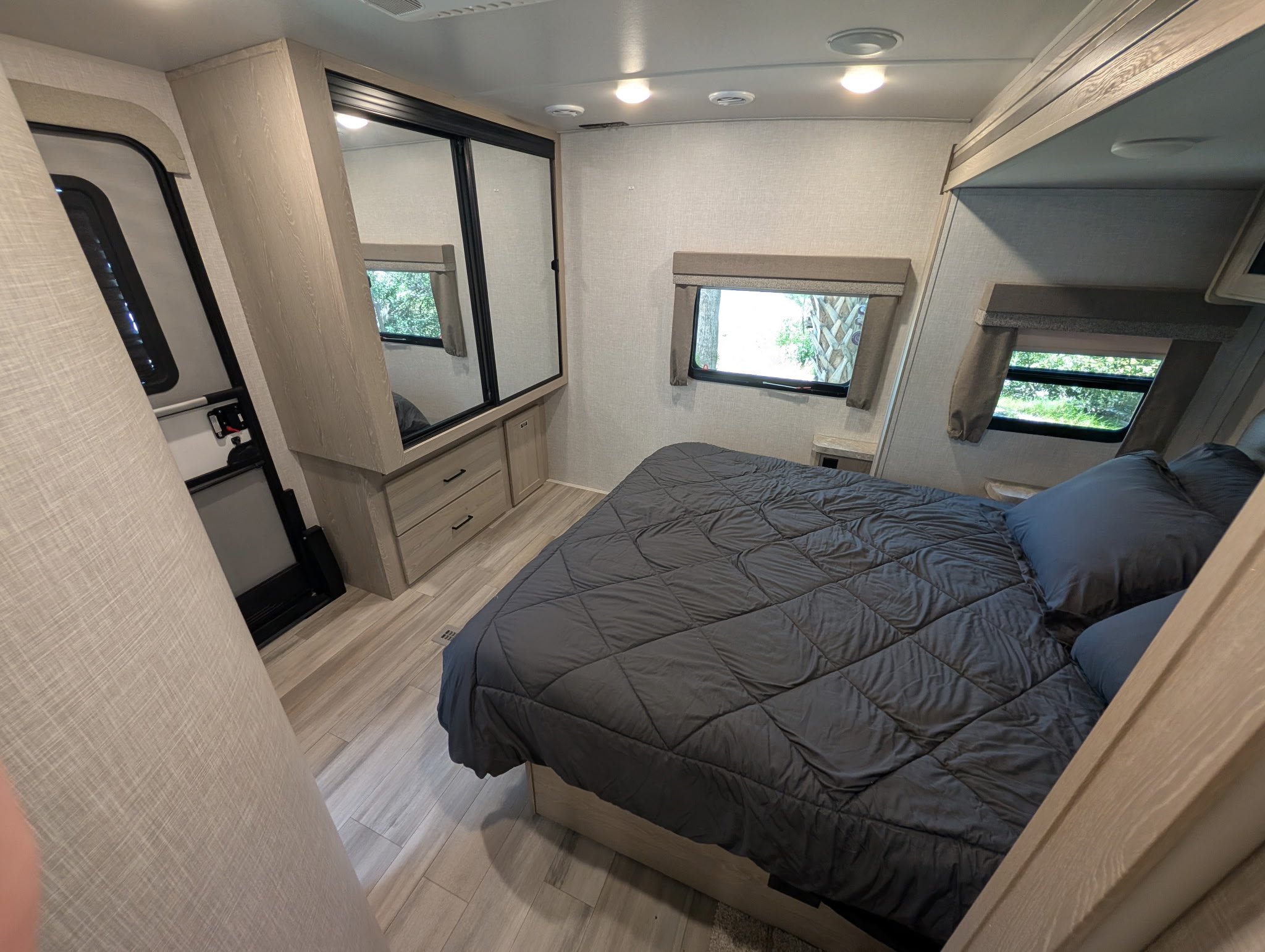 Bright RV rental bedroom featuring a dark gray bed, mirrored wardrobe, light wood accents, and sunlit windows.. Forest River Flagstaff Super Lite 2022