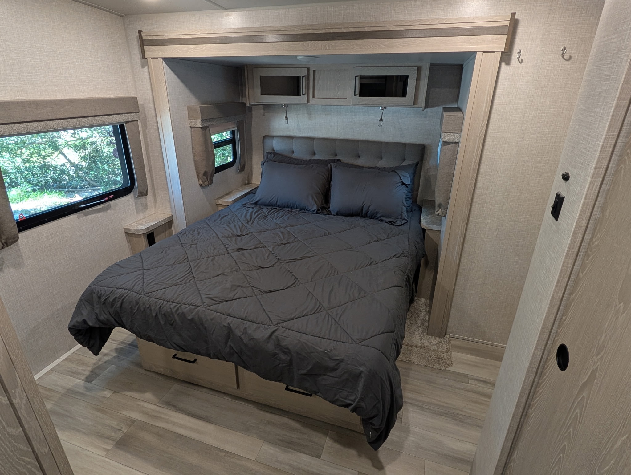 This RV rental bedroom features a comfy queen bed with gray bedding, built-in storage, and windows overlooking nature.. Forest River Flagstaff Super Lite 2022