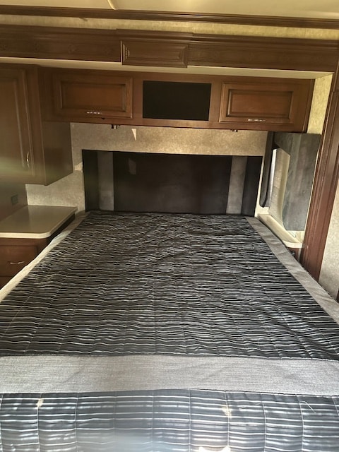 RV rental bedroom with a cozy bed, dark patterned comforter, overhead cabinets, and wood accents.. Fleetwood expedition 2011