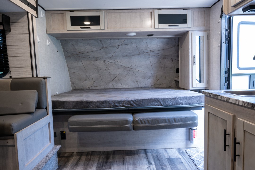 Modern rv rental interior: cozy bed, light wood cabinets, and kitchenette, ready for your trip.. Keystone RV Sunset Trail 2023