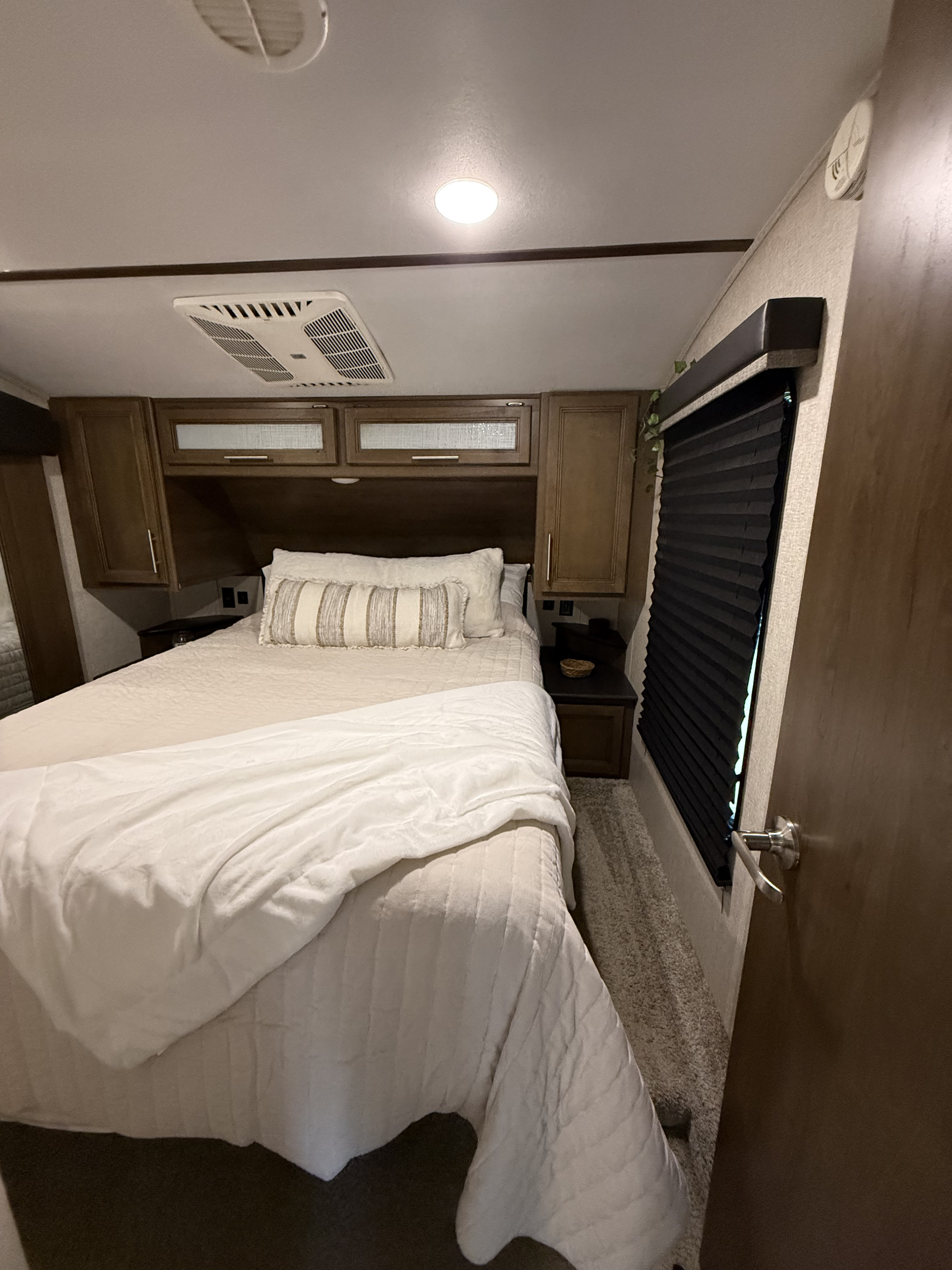 Cozy RV rental bedroom with comfortable bed, overhead cabinets, AC unit, and natural light from window.. Keystone RV Cougar 2021
