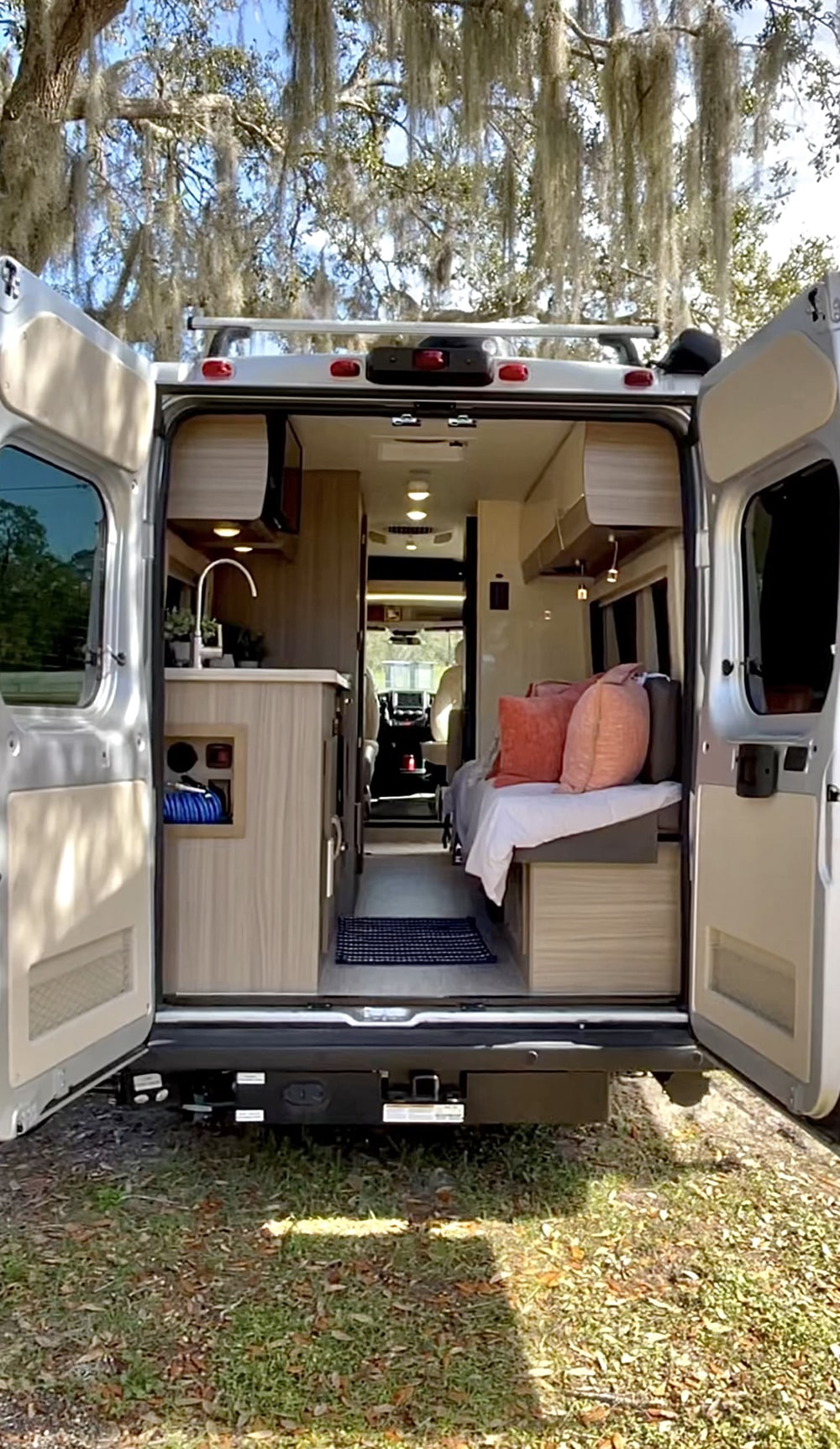 Back doors open on a cozy RV rental. Modern camper van interior features a kitchen, bed area, and path to the front cabin.. Jayco Swift 2021