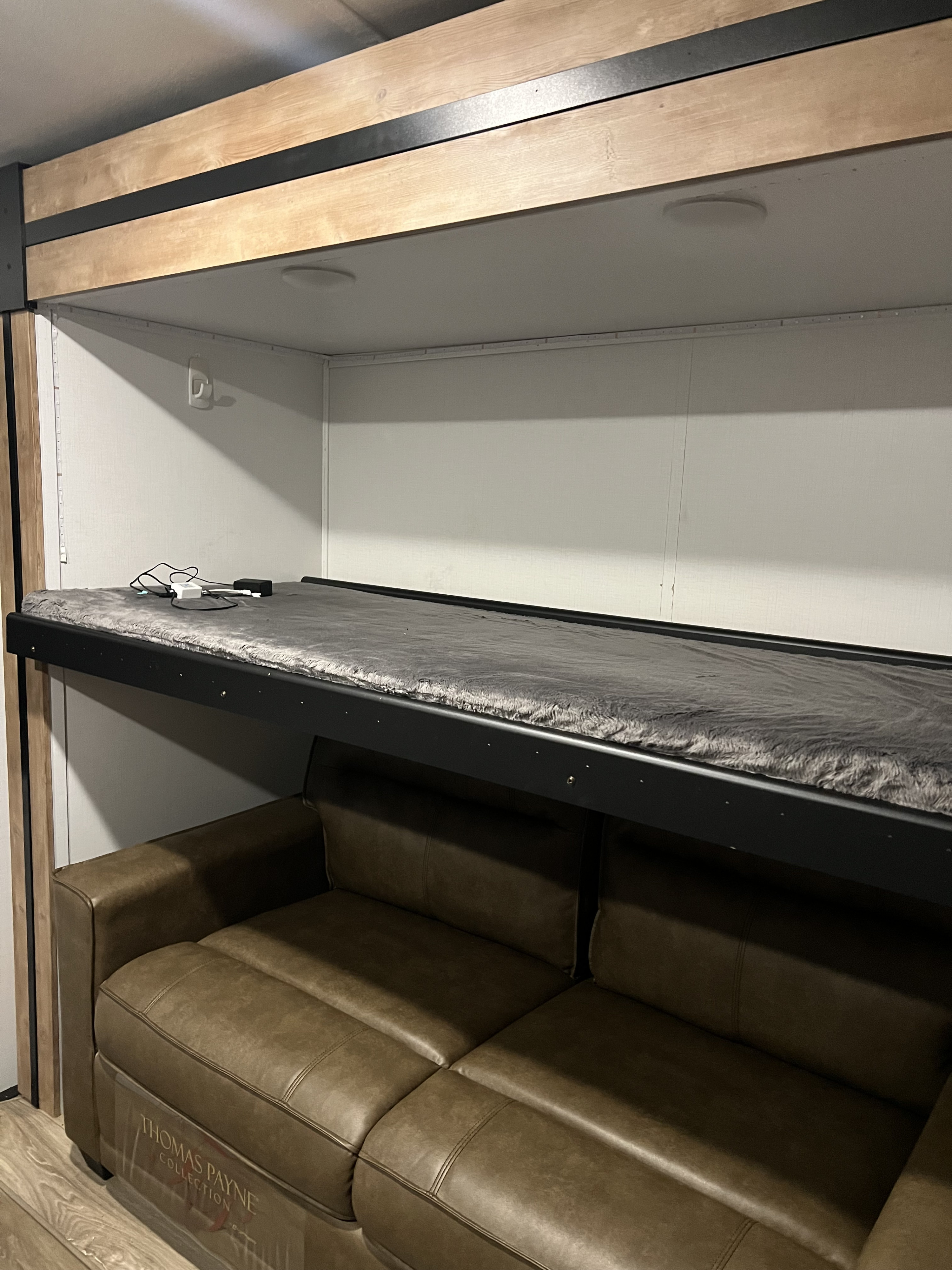 RV rental bunk area with a cozy grey mattress above a brown leather sofa. Charging station on bunk.. Keystone RV Outback 2022