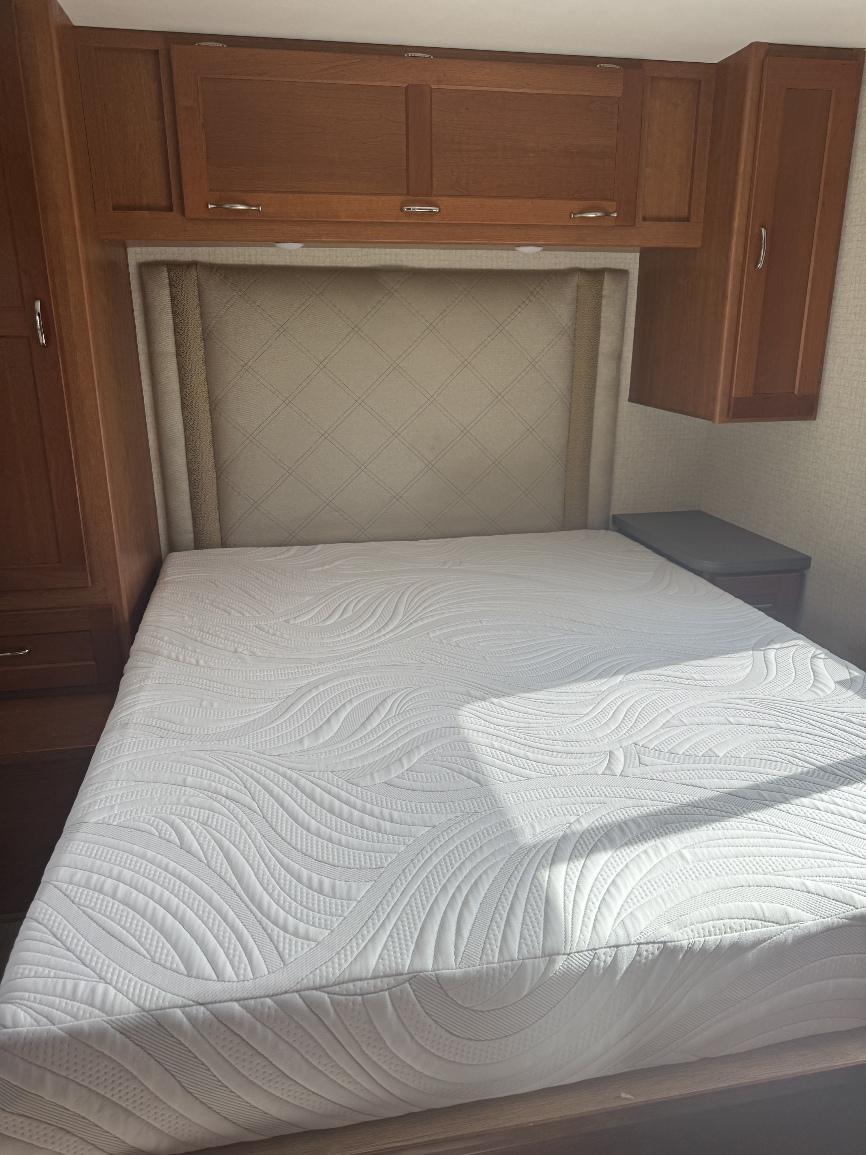 Inside an RV rental: a pristine bed with wave-patterned mattress, beige headboard, and wood cabinetry.. Winnebago Other 2016