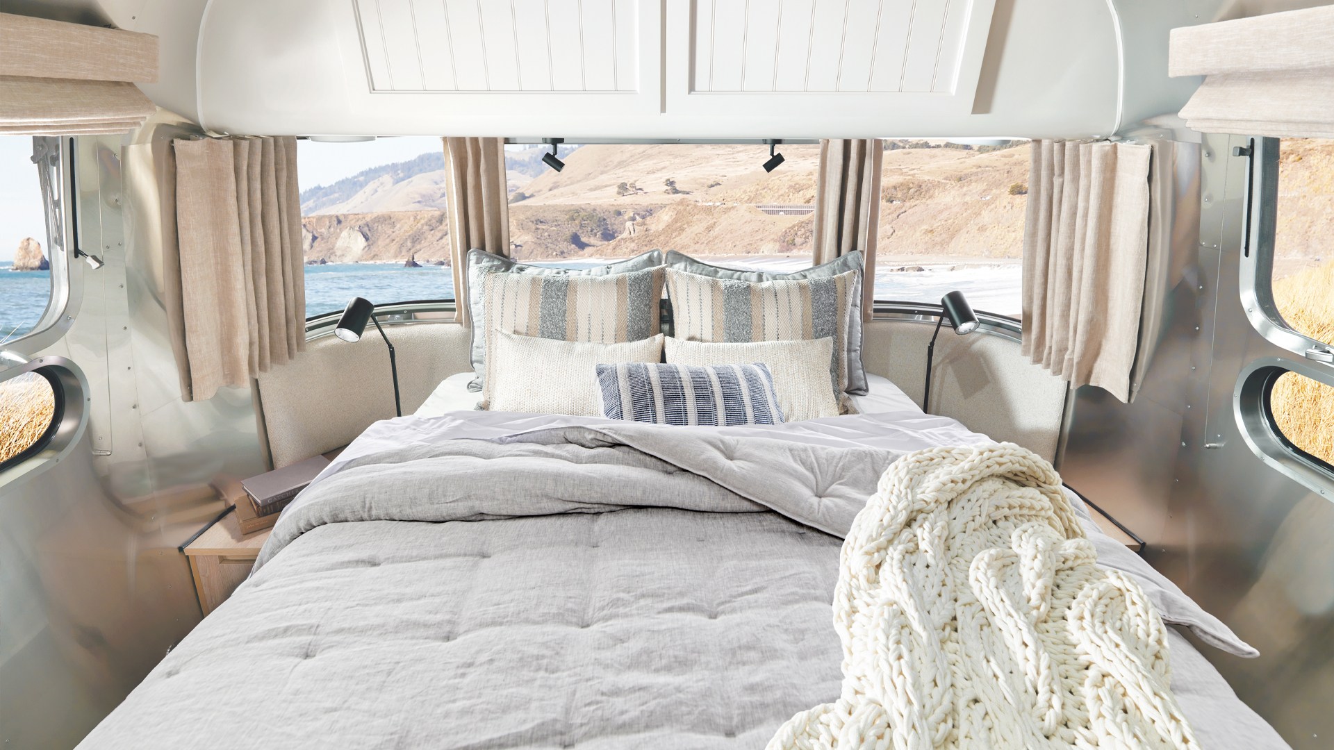 Stunning ocean view from this cozy RV rental bedroom, featuring a comfortable bed, pillows, and a chunky knit blanket.. Airstream Pottery Barn 2024